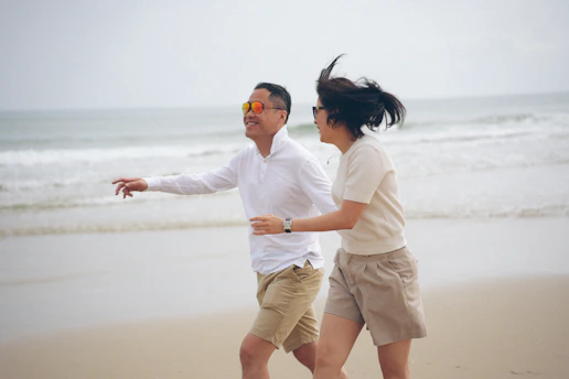 A couple running on a sandy beach near the ocean.