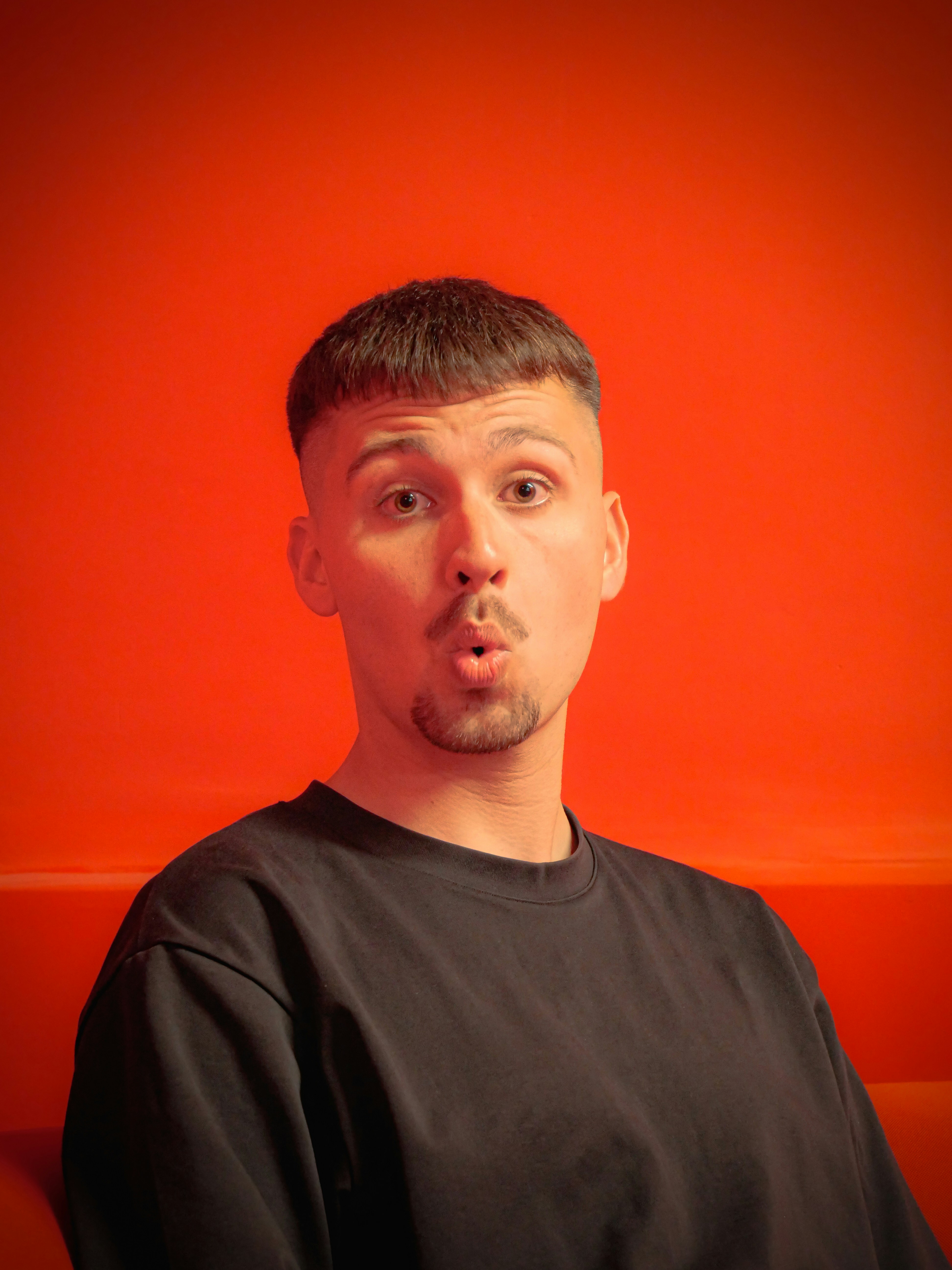 Mann mit überraschtem Gesichtsausdruck vor orangefarbenem Hintergrund