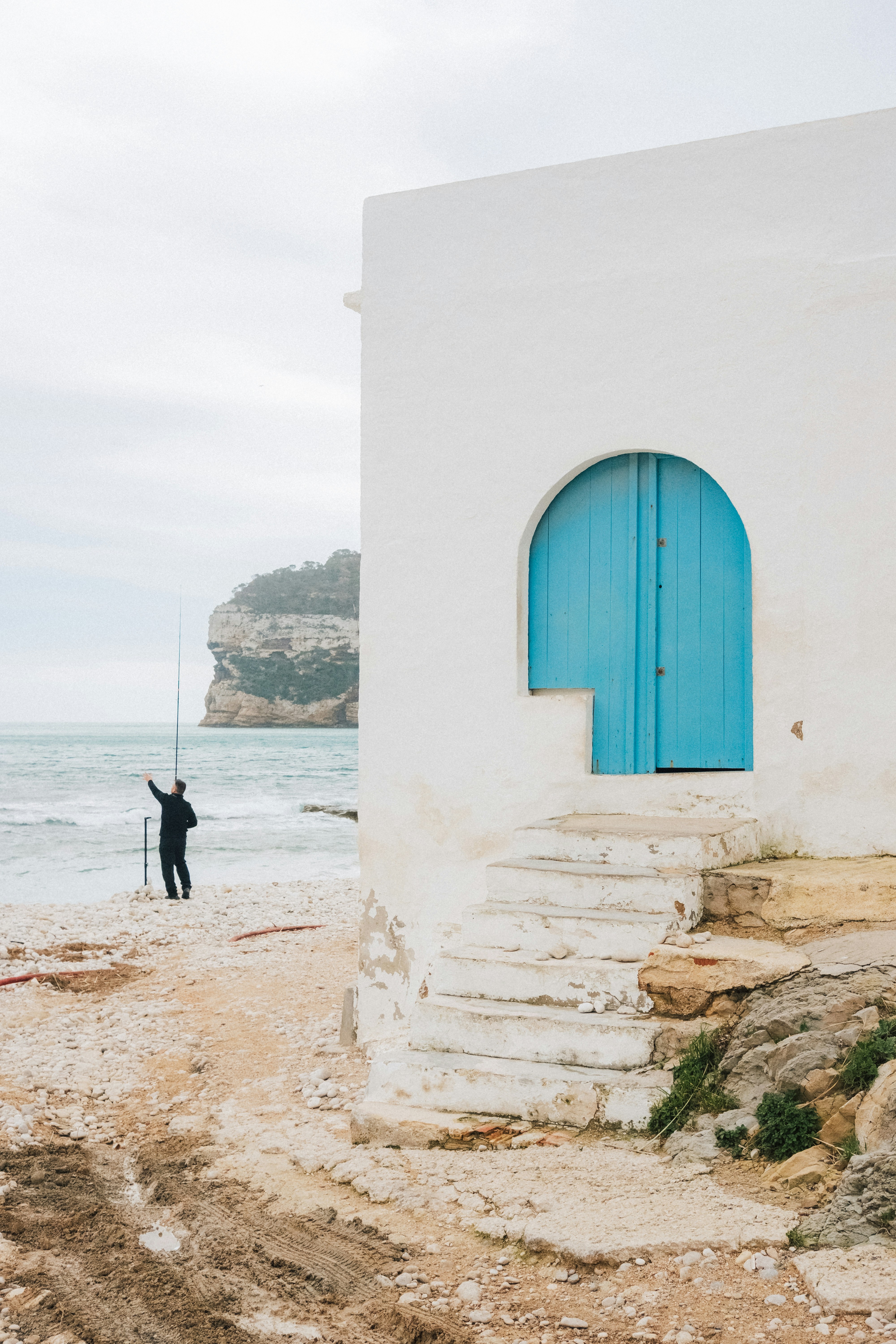 Mann angelt an einem felsigen Strand neben einem weißen Gebäude
