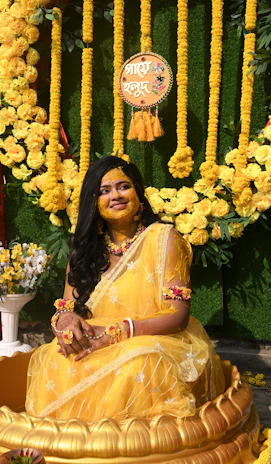 A woman in a yellow saree decorated with turmeric paste.