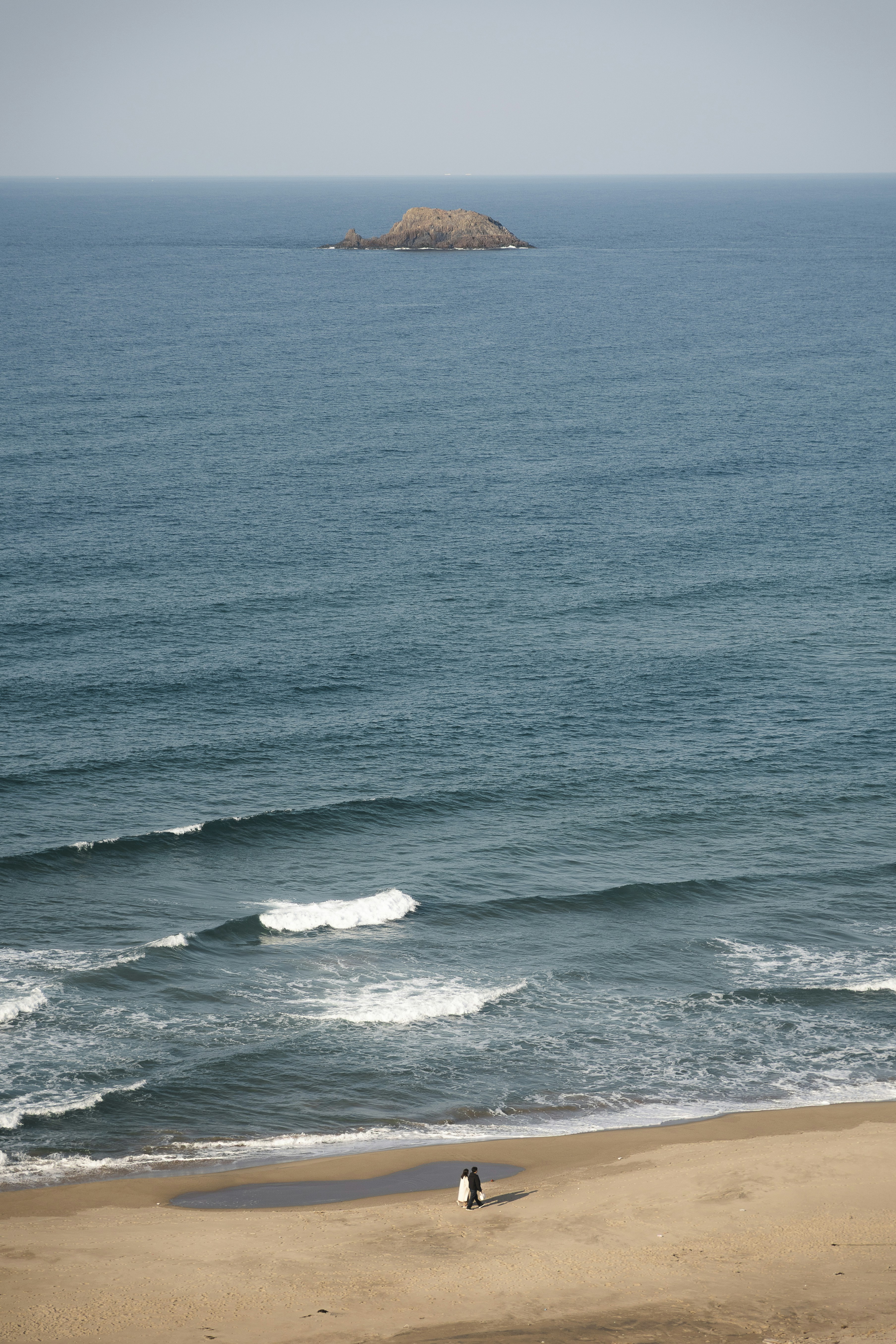 Couple walking on a sandy beach with ocean waves.