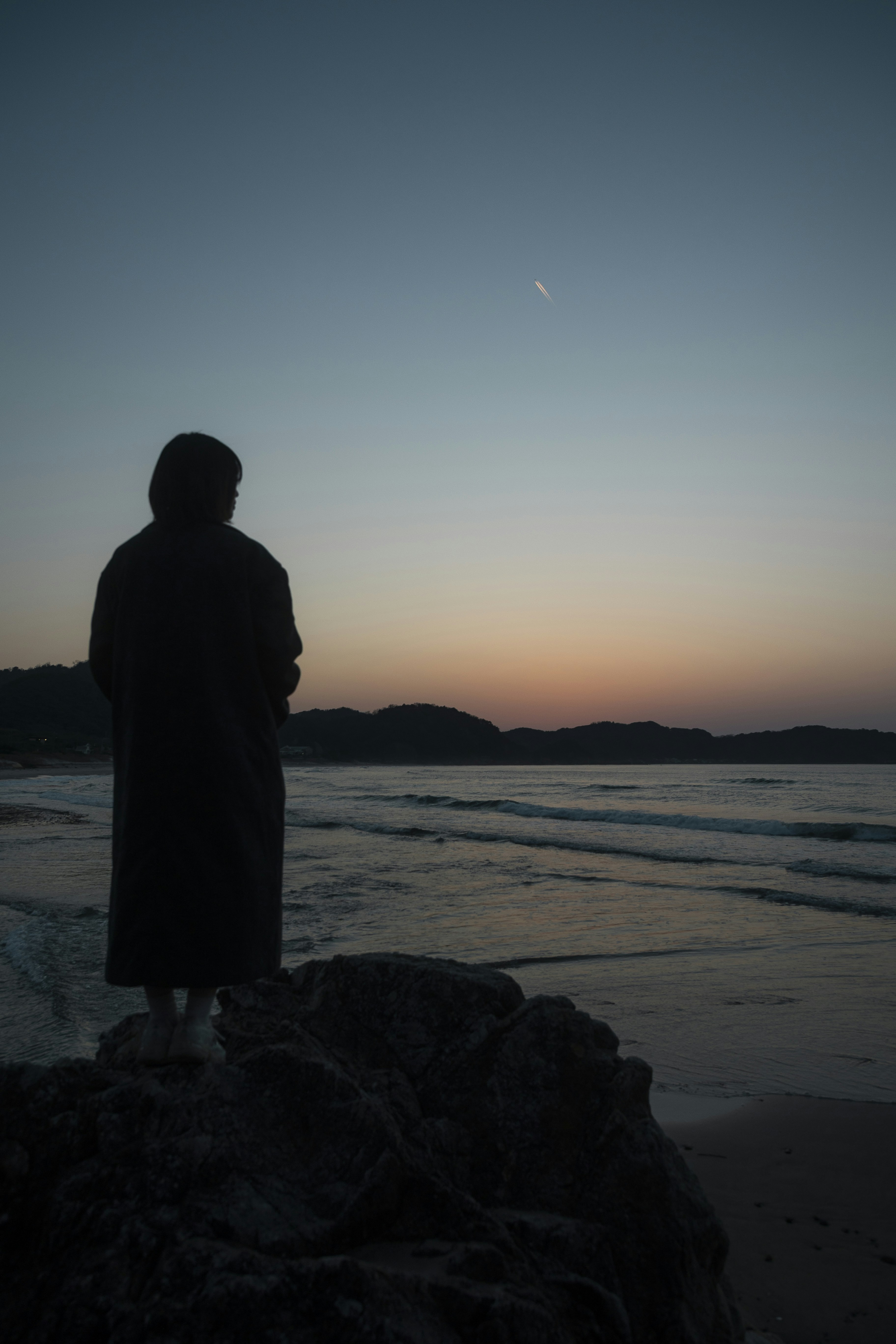 Silhouette of person watching sunset over ocean waves.
