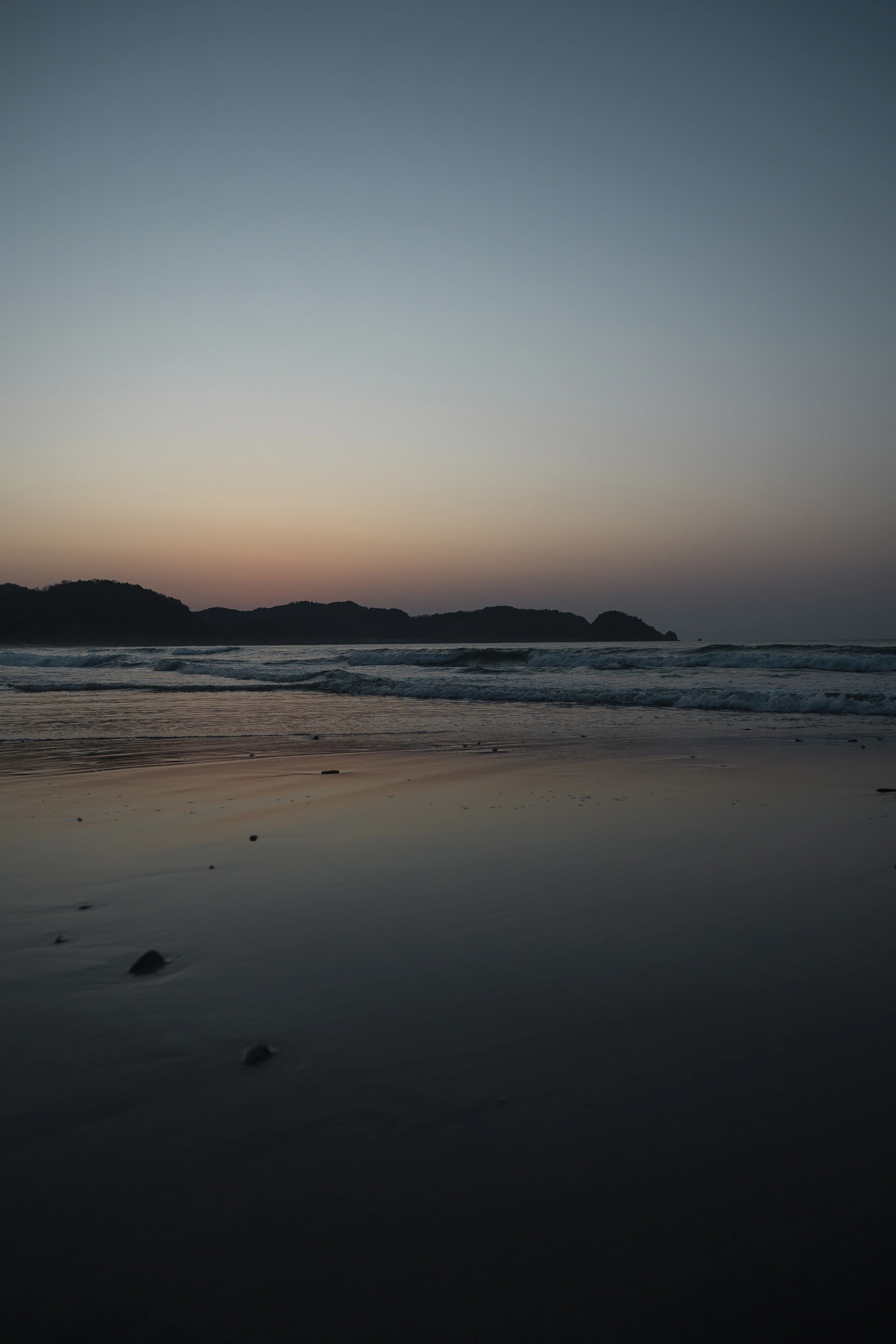 Calm ocean waves on a sandy beach at dusk.