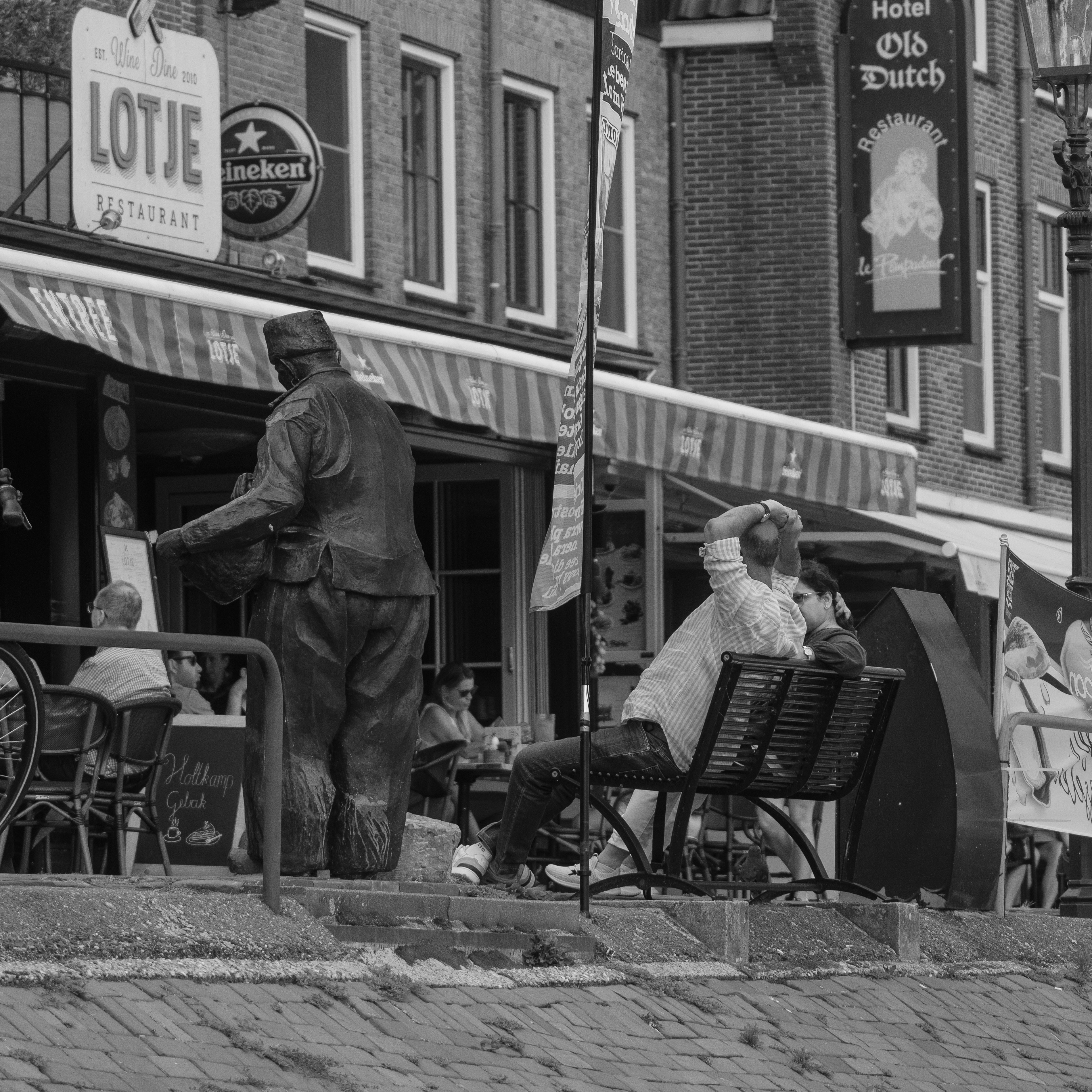 People relax outside a canal-side cafe with a statue.