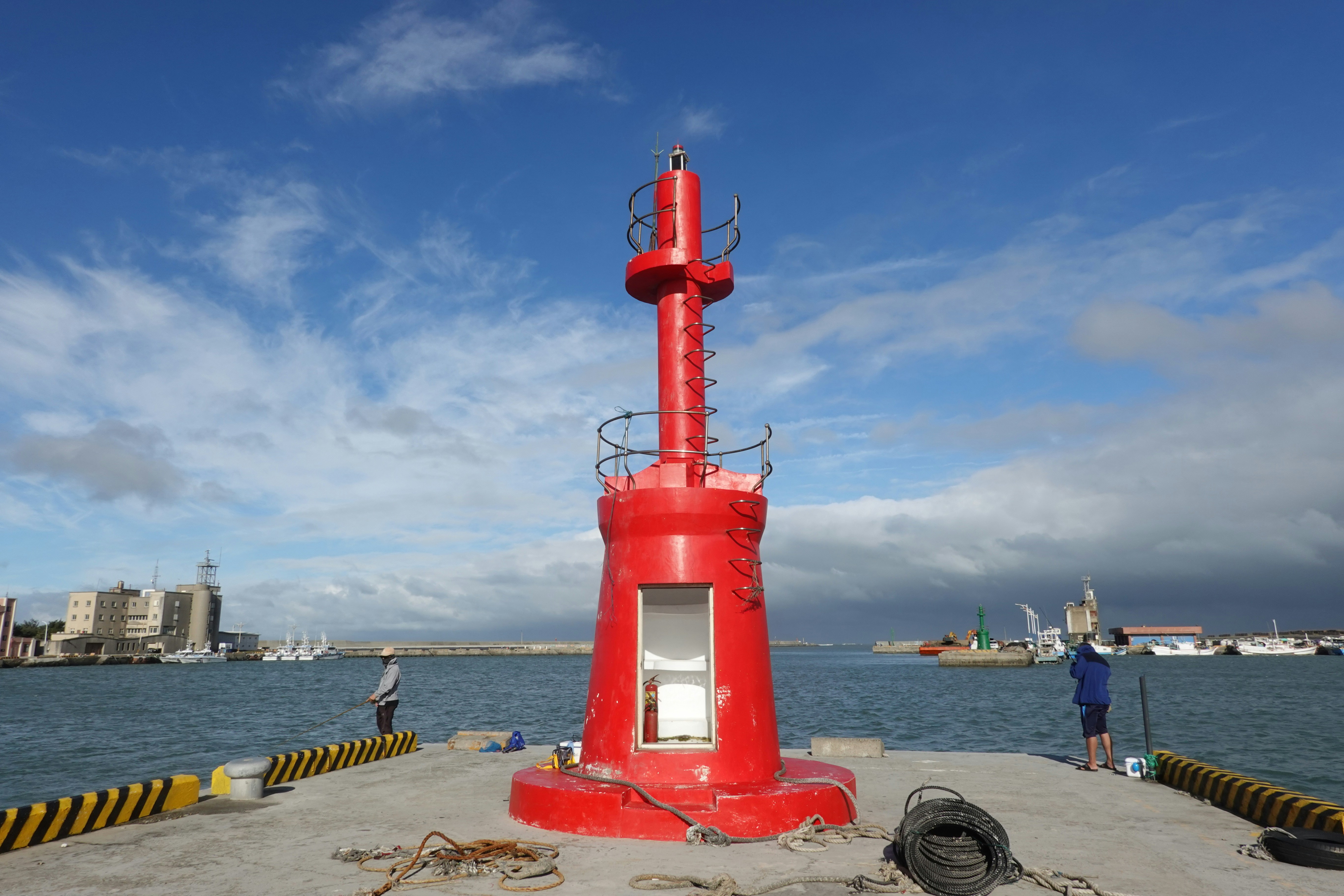A red lighthouse stands on a pier by the sea.