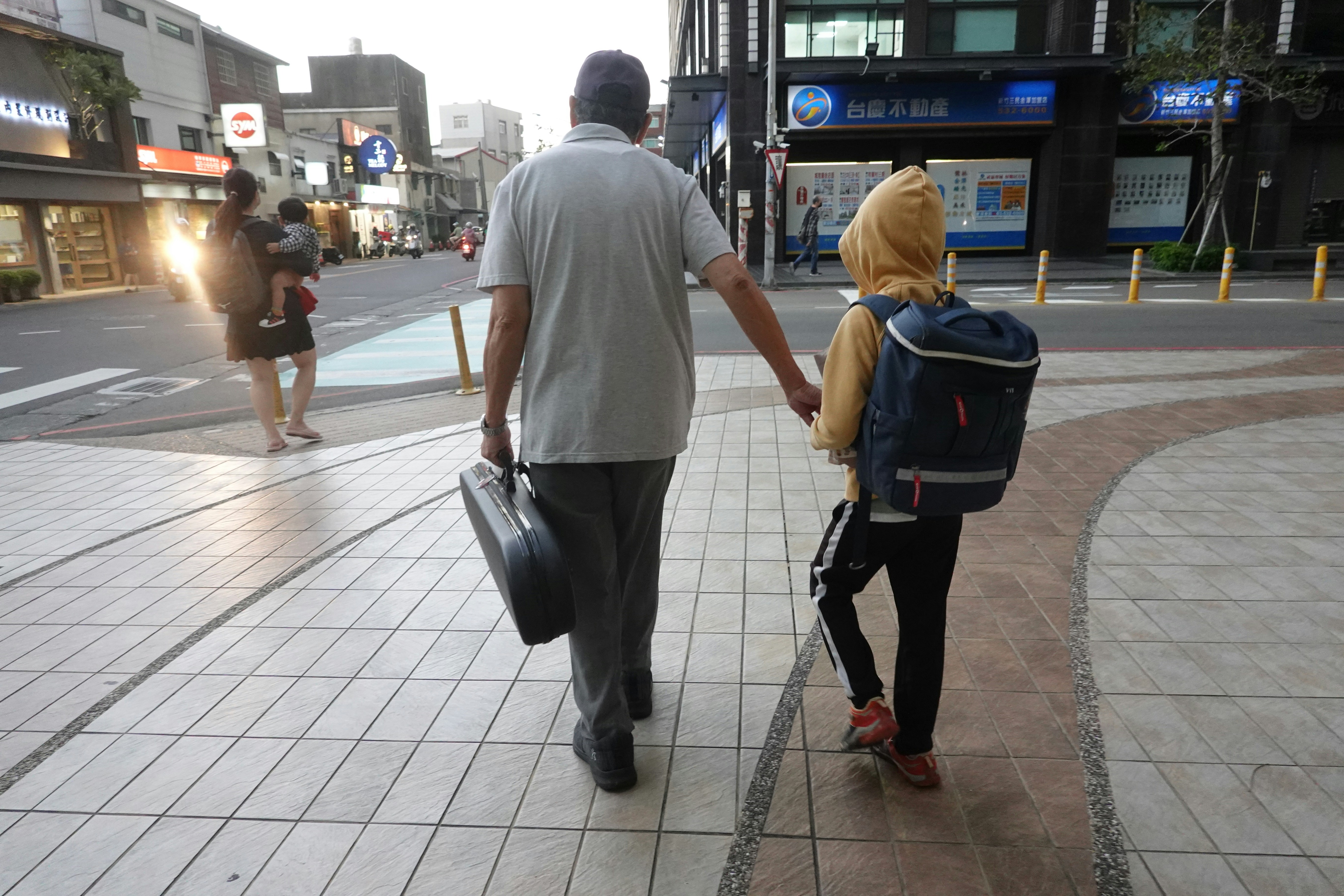 Man and child walk hand-in-hand on sidewalk.