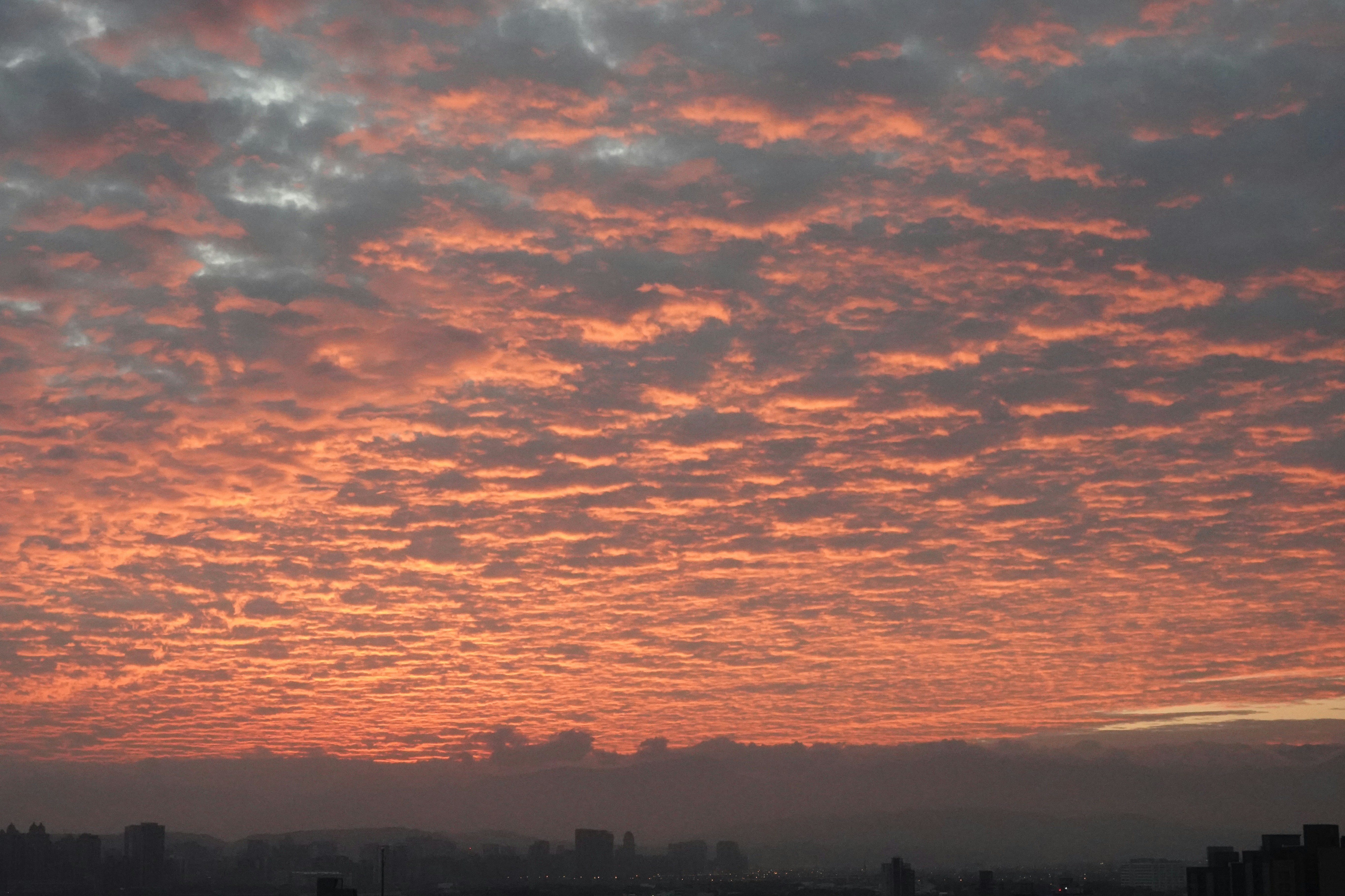Fiery sunset sky with scattered clouds over cityscape.