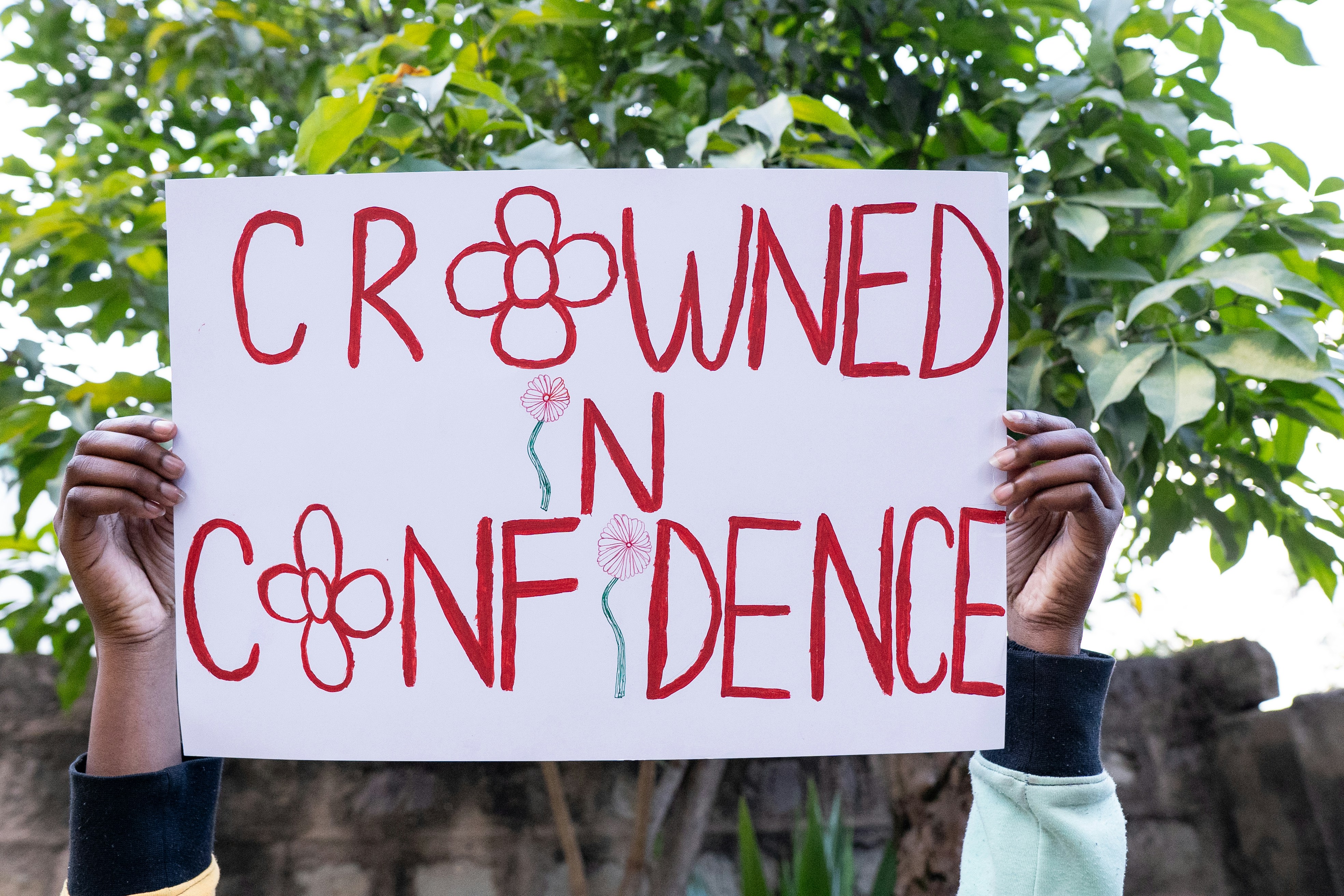Hände halten ein Schild mit der Aufschrift "gekrönt in Vertrauen"