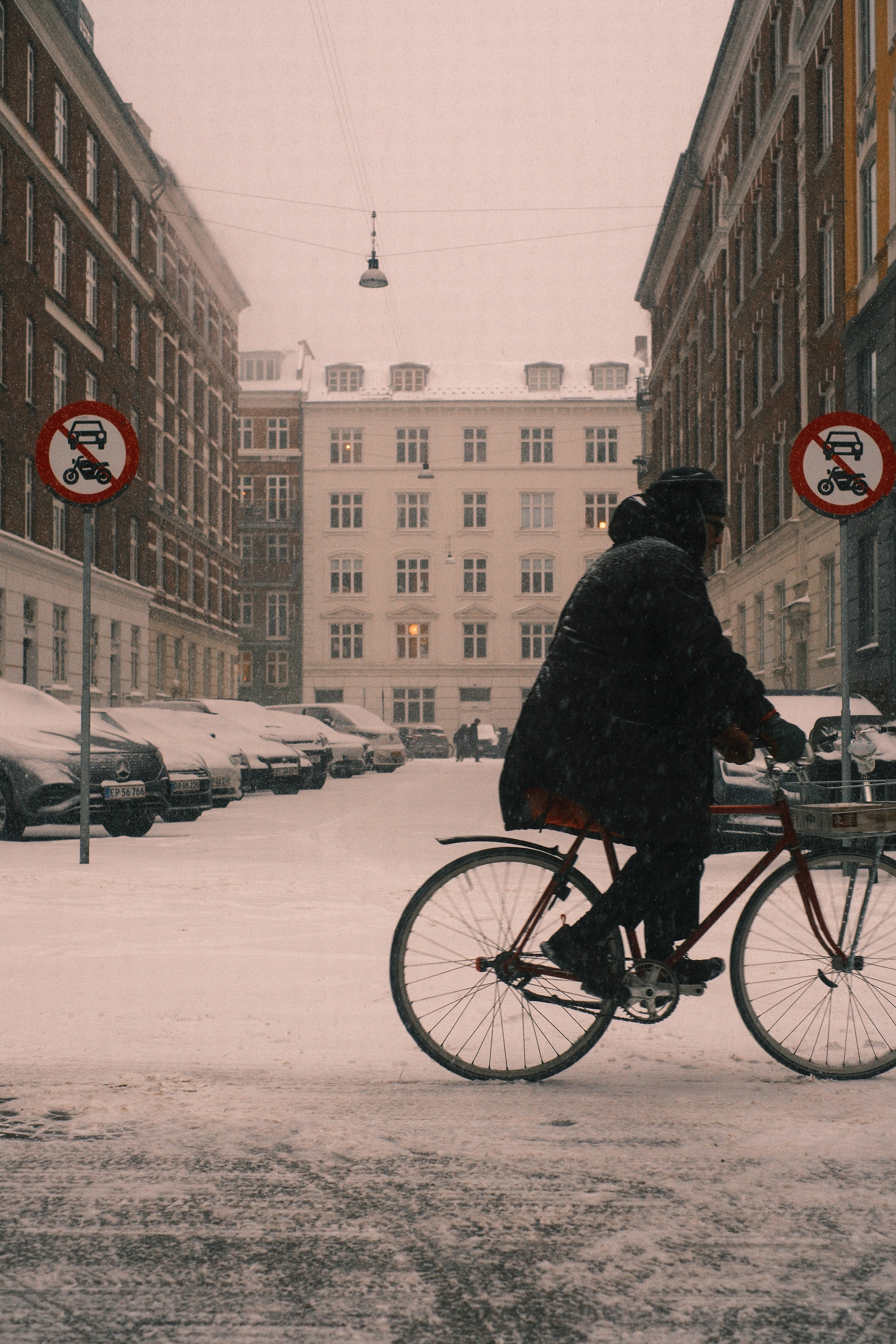 Person rides bicycle on snowy city street during snowfall.