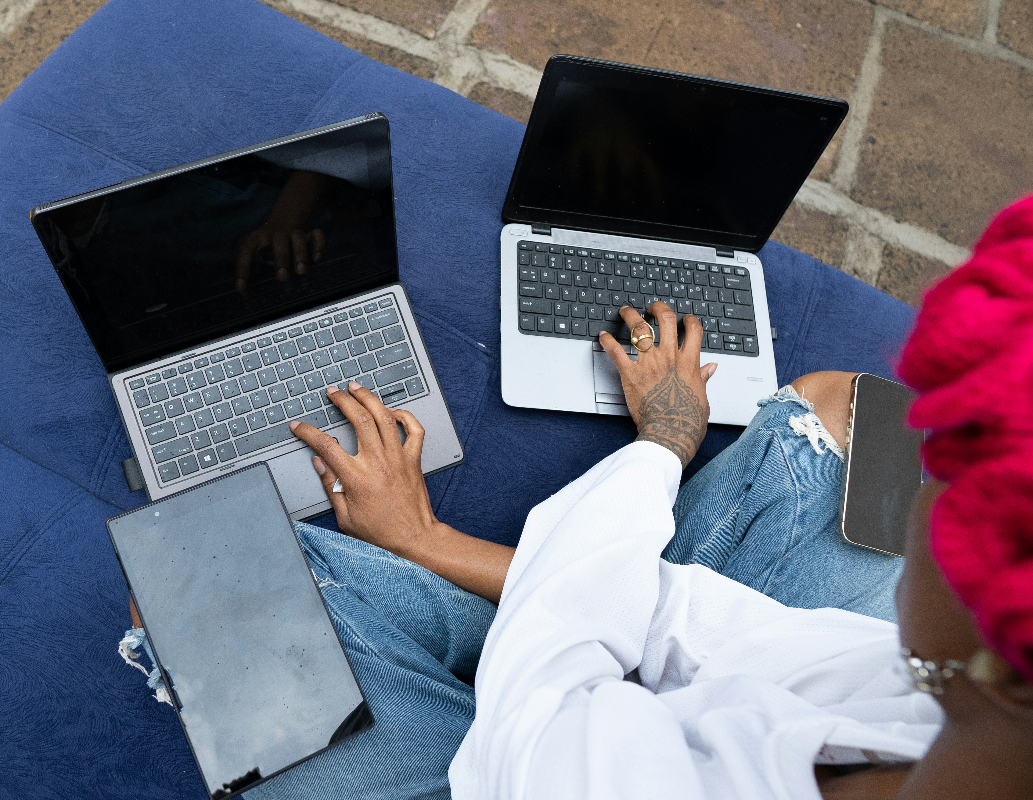 Dos personas usando portátiles al aire libre sobre un cojín azul.