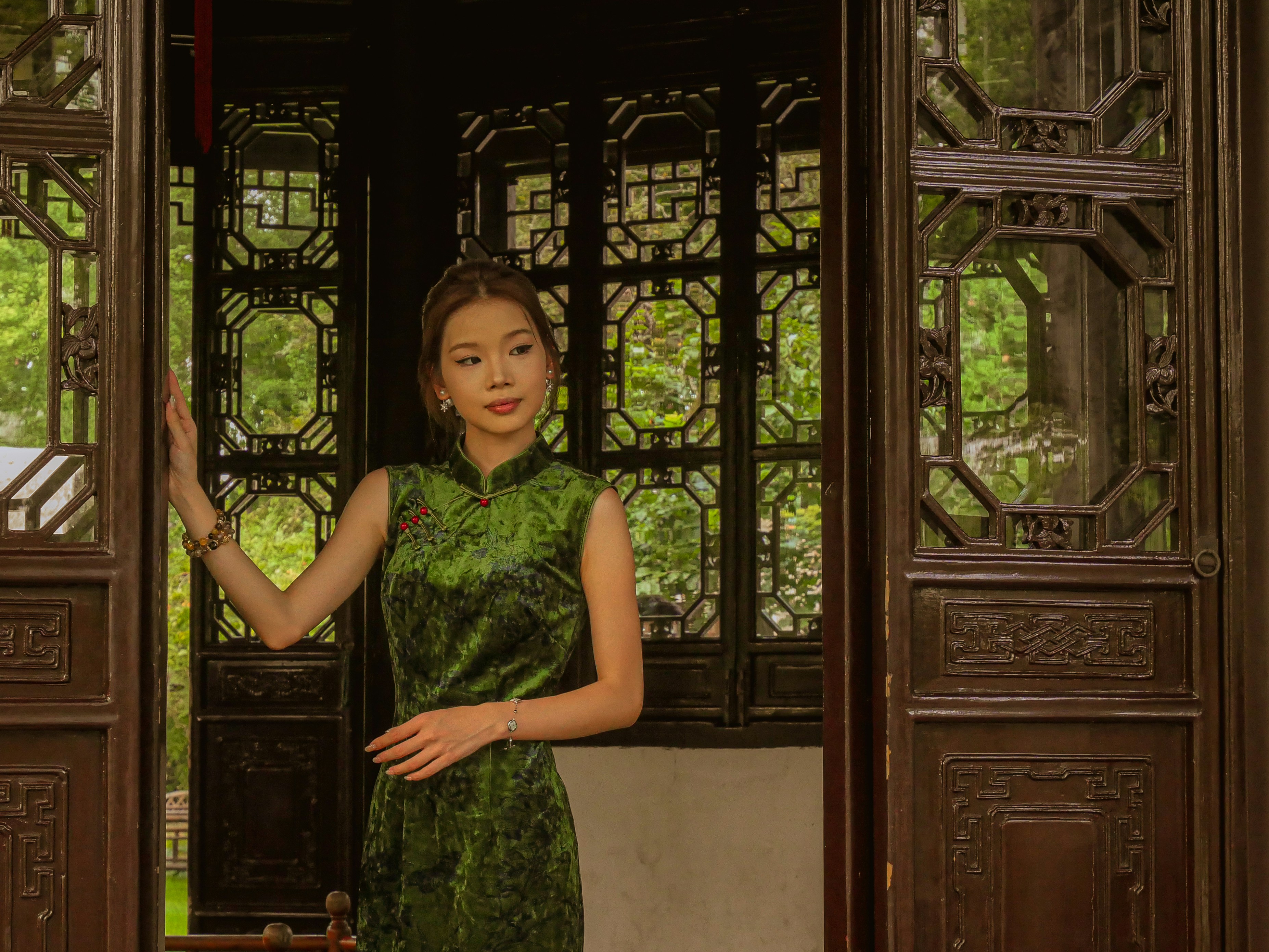 Woman in green dress stands by ornate wooden doorway.