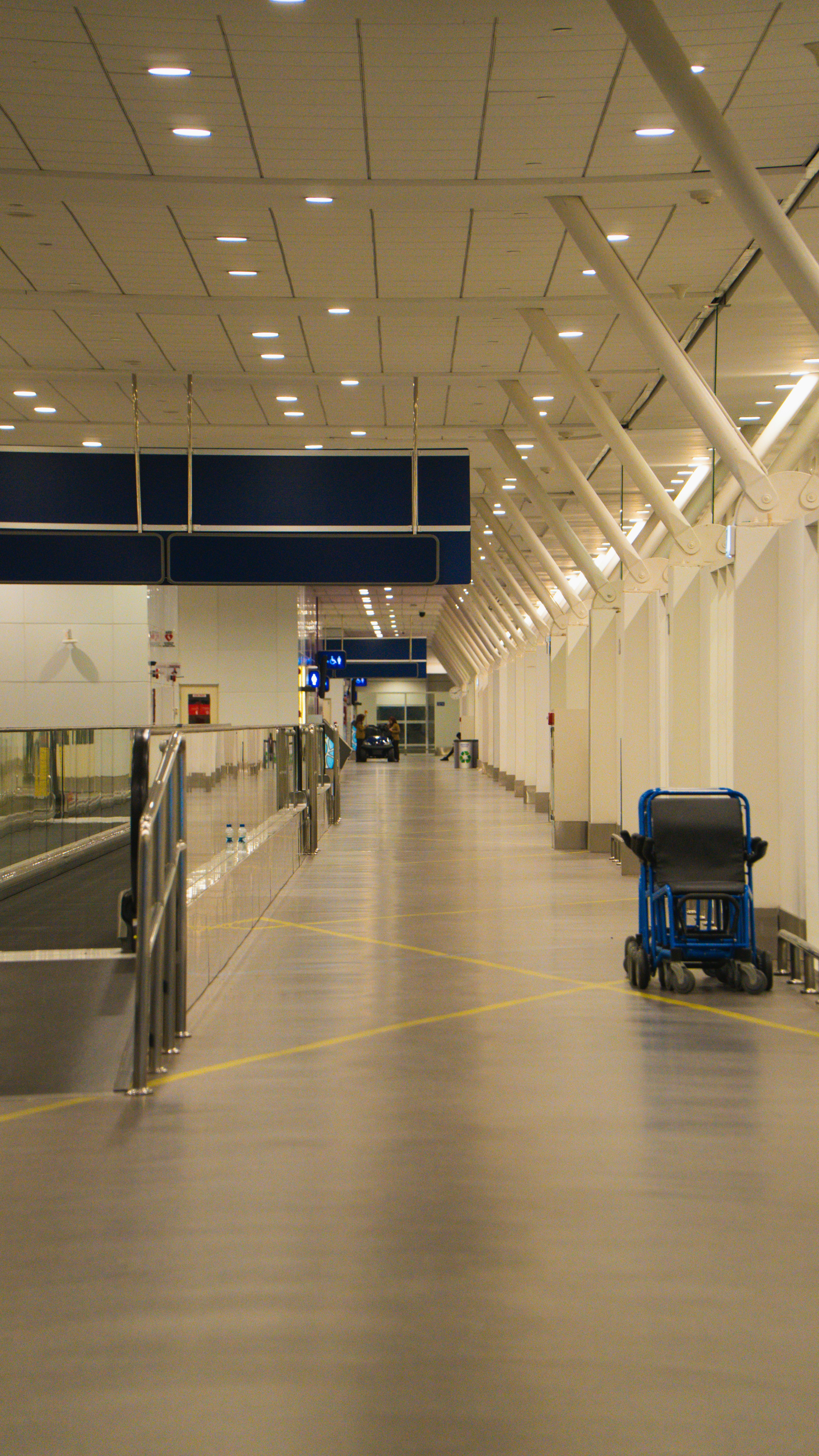 Modern airport walkway with a blue luggage cart.