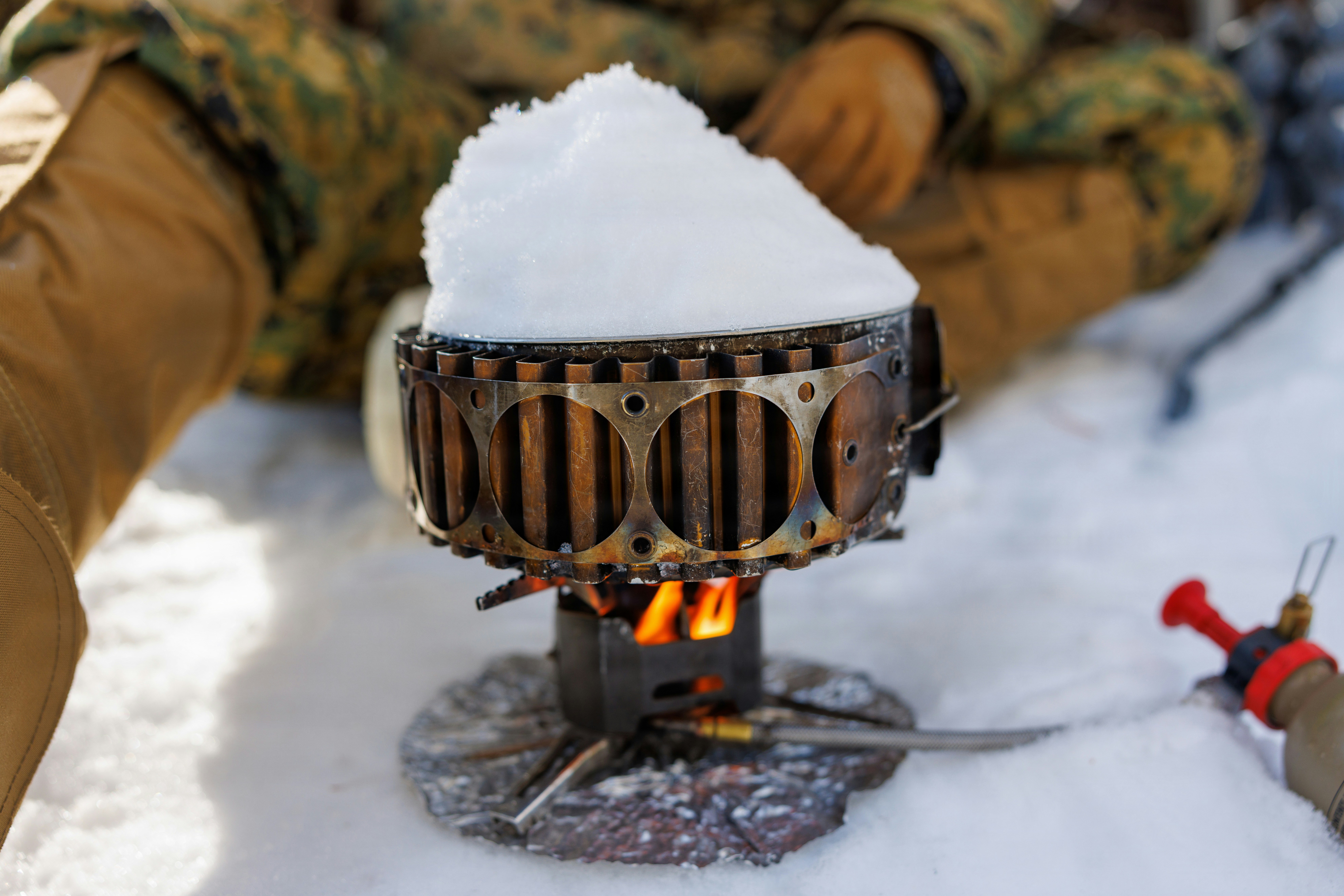 A portable stove melts snow with a flame.