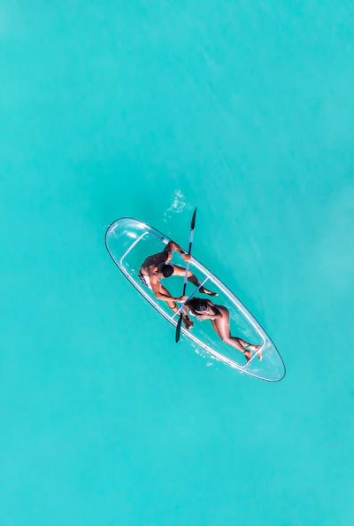 Couple paddling a clear kayak on turquoise water.