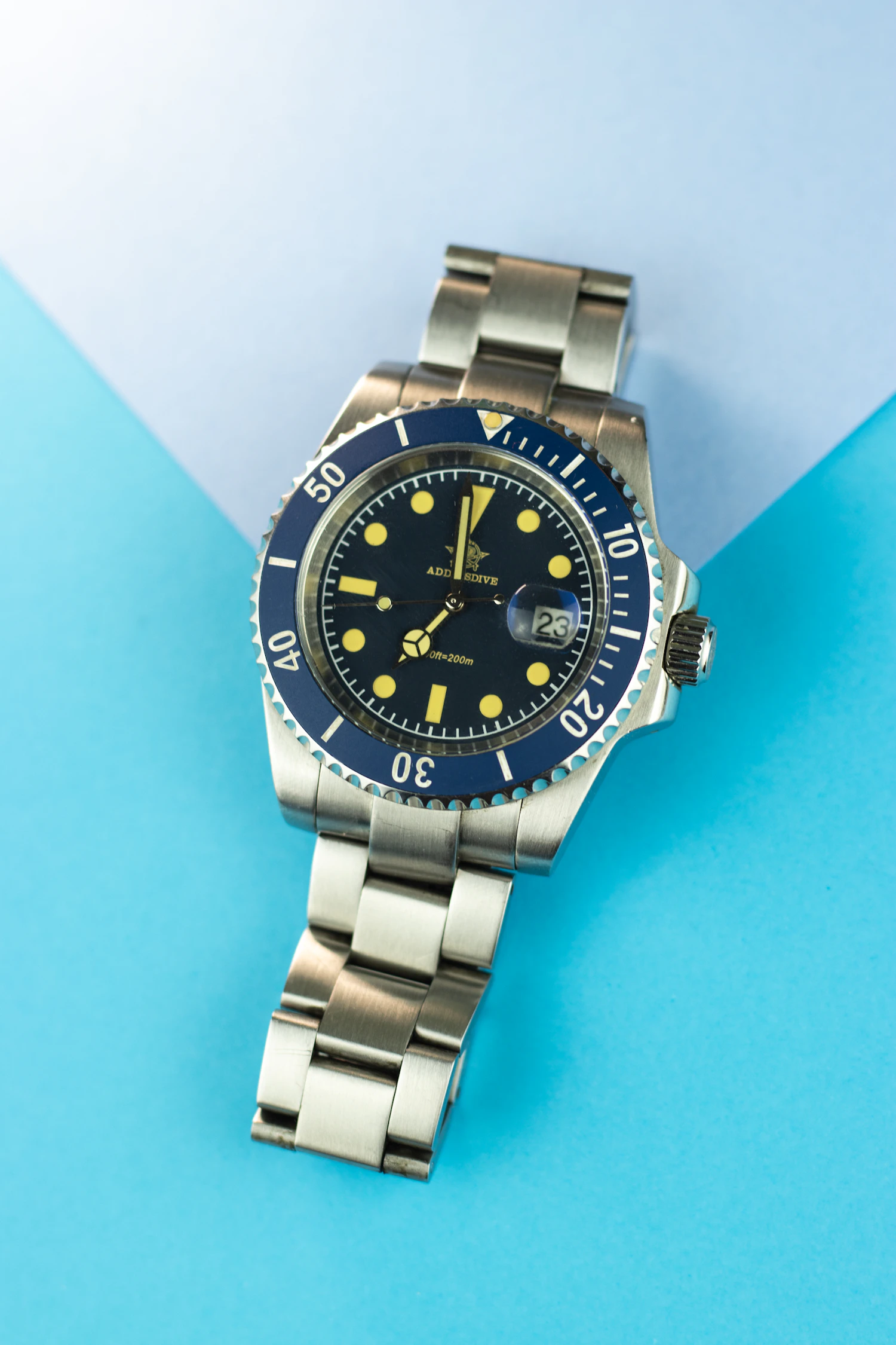 Doubs 40, a navy diver with gilt markers and a navy bezel on a steel bracelet, on blue paper — low stock, two left