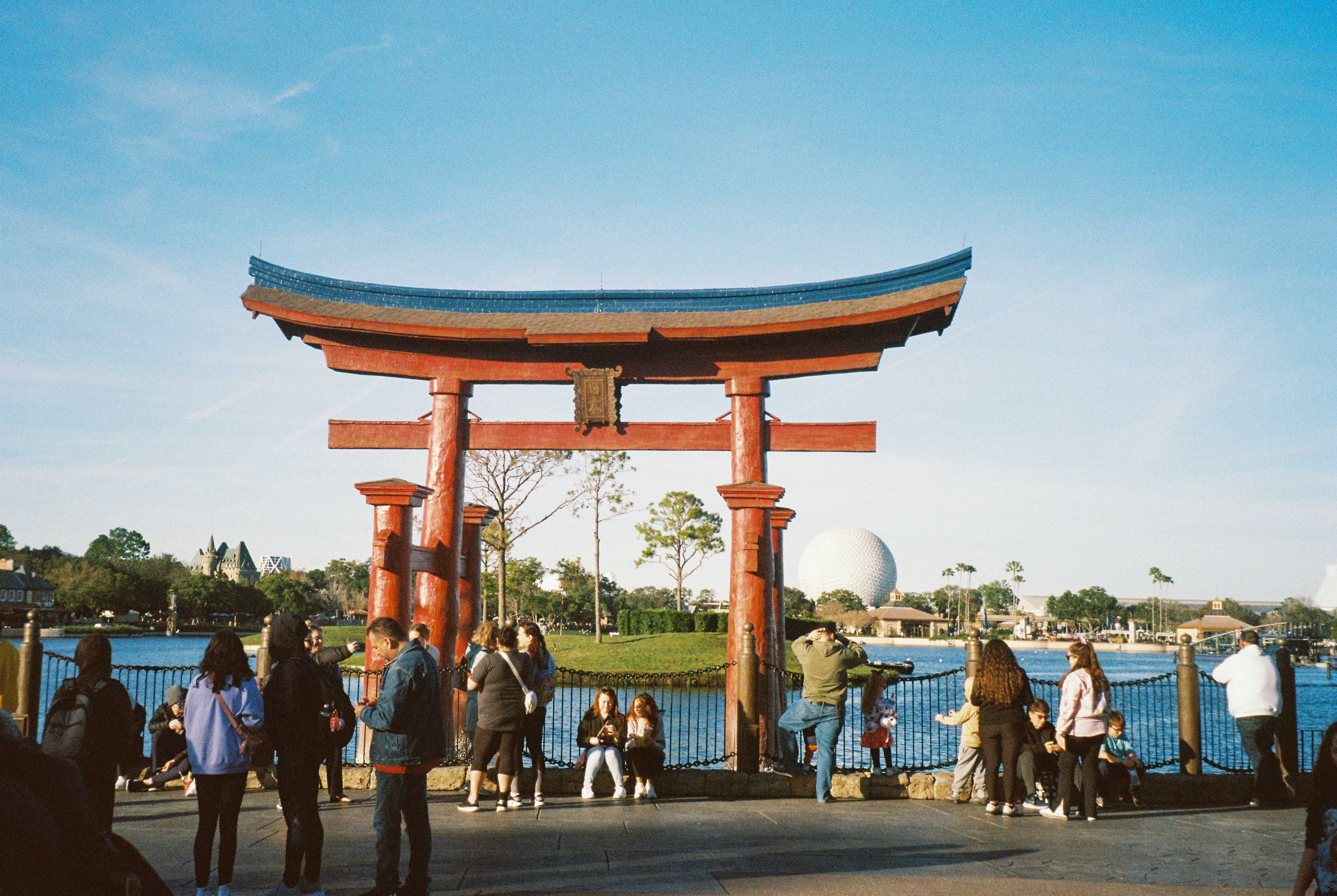 People gathered near a large red torii gate by water
