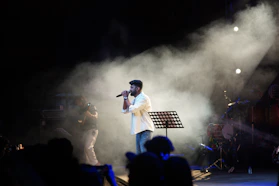 A man sings on stage with smoke and lights.