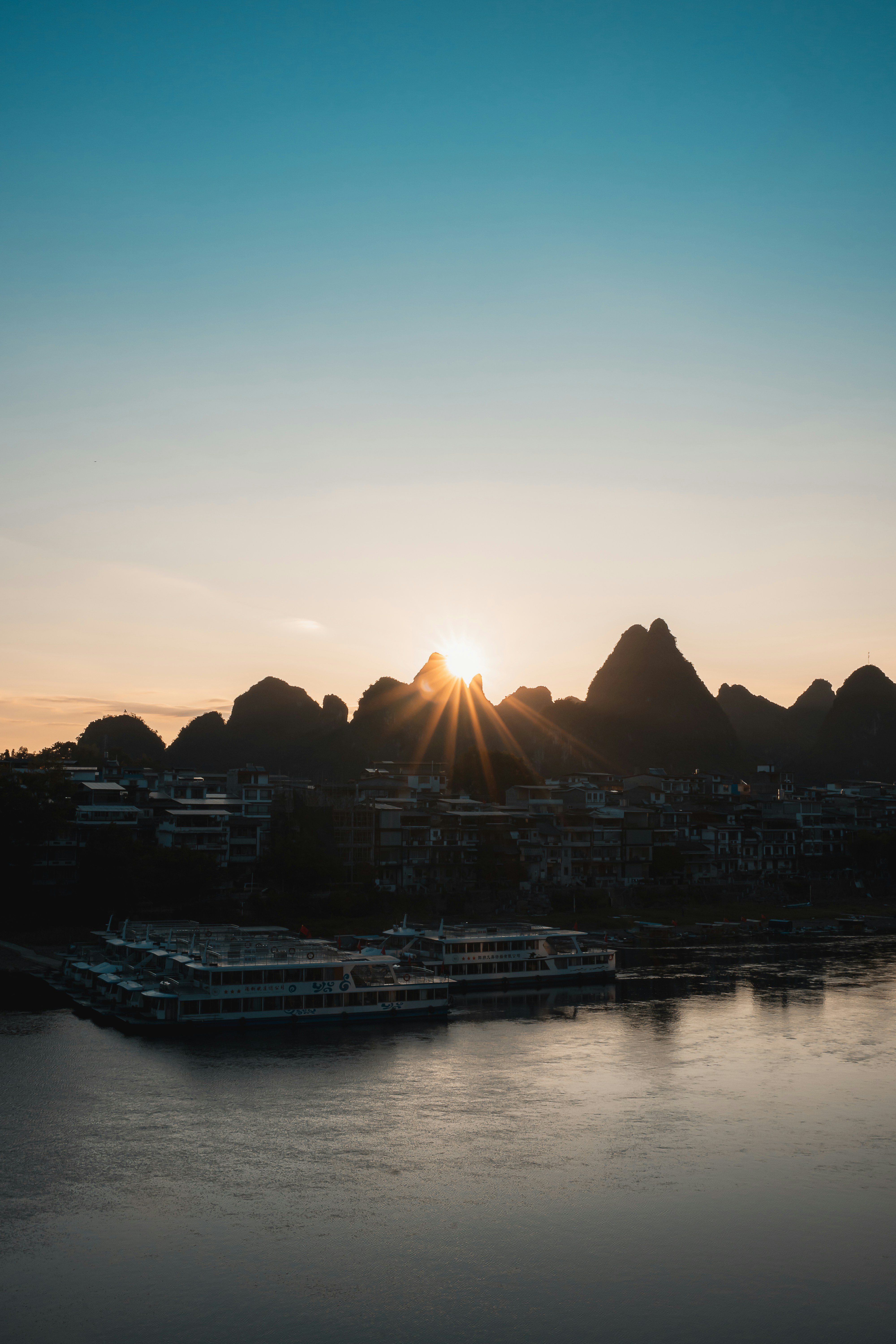 Sunset over a river with karst mountains and boats.