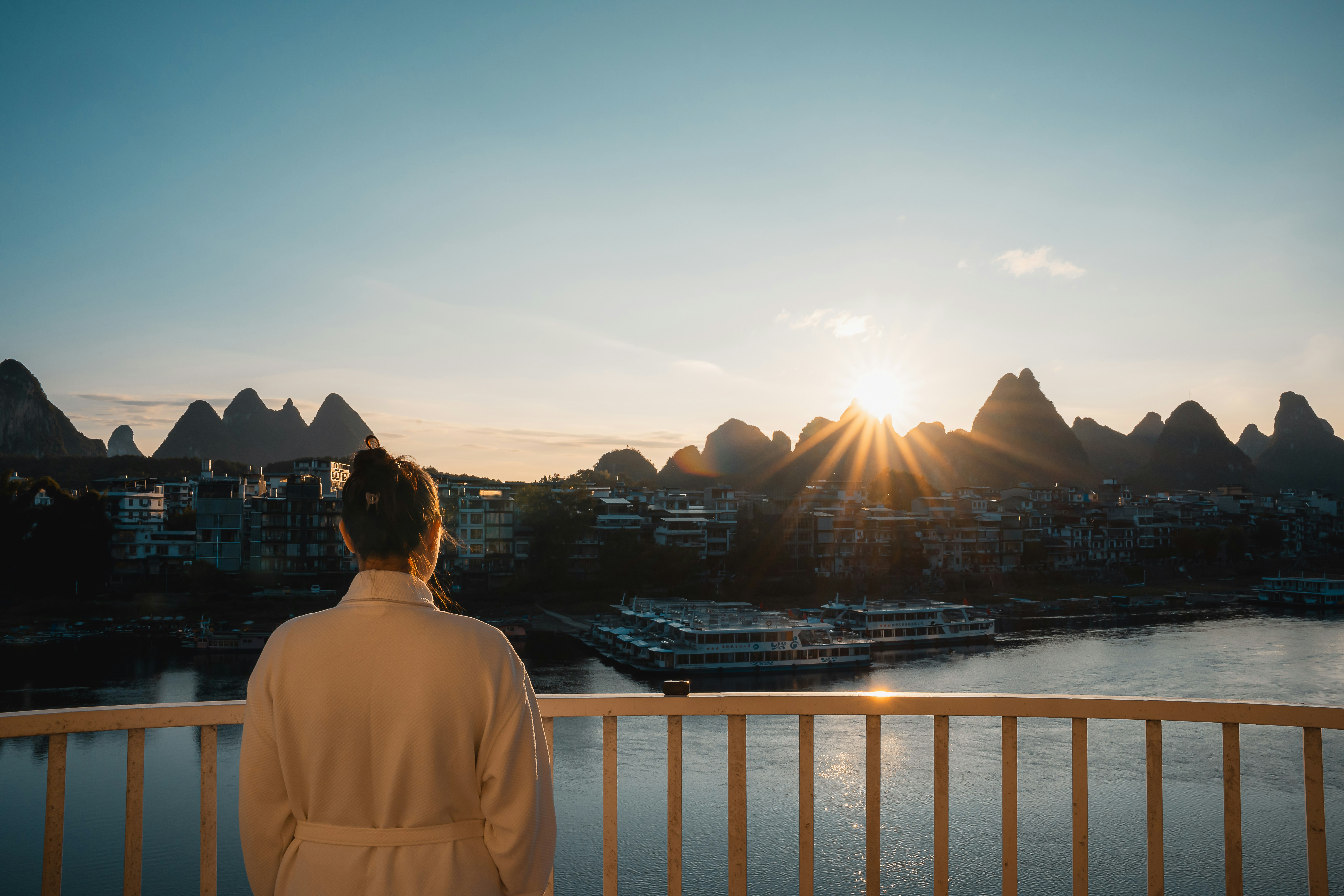 Woman in bathrobe watches sunrise over karst mountains