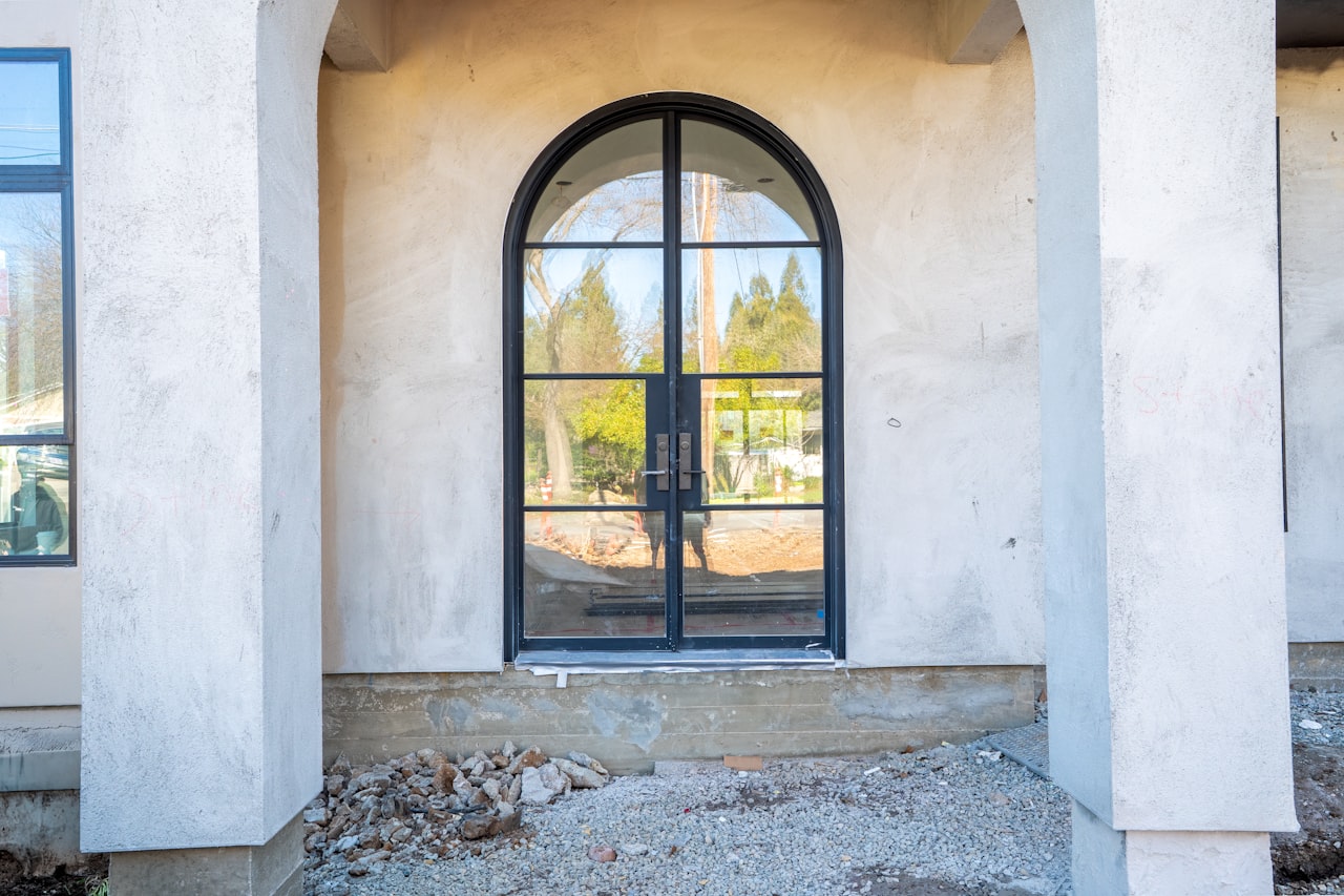 Arched stone entryway with double glass doors, symmetrical topiary planters, and elegant outdoor sconces on a Northern California luxury estate in Placer County