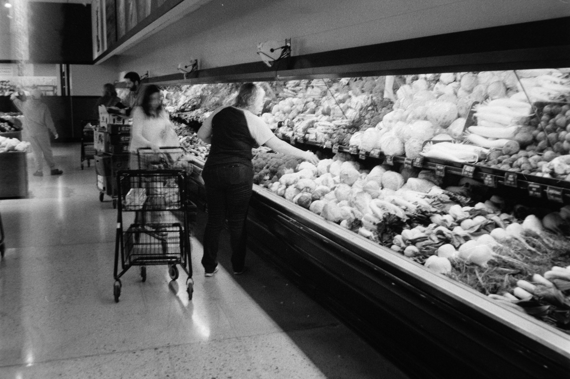 Black-and-white photo of shoppers with carts in the produce aisle of a grocery store