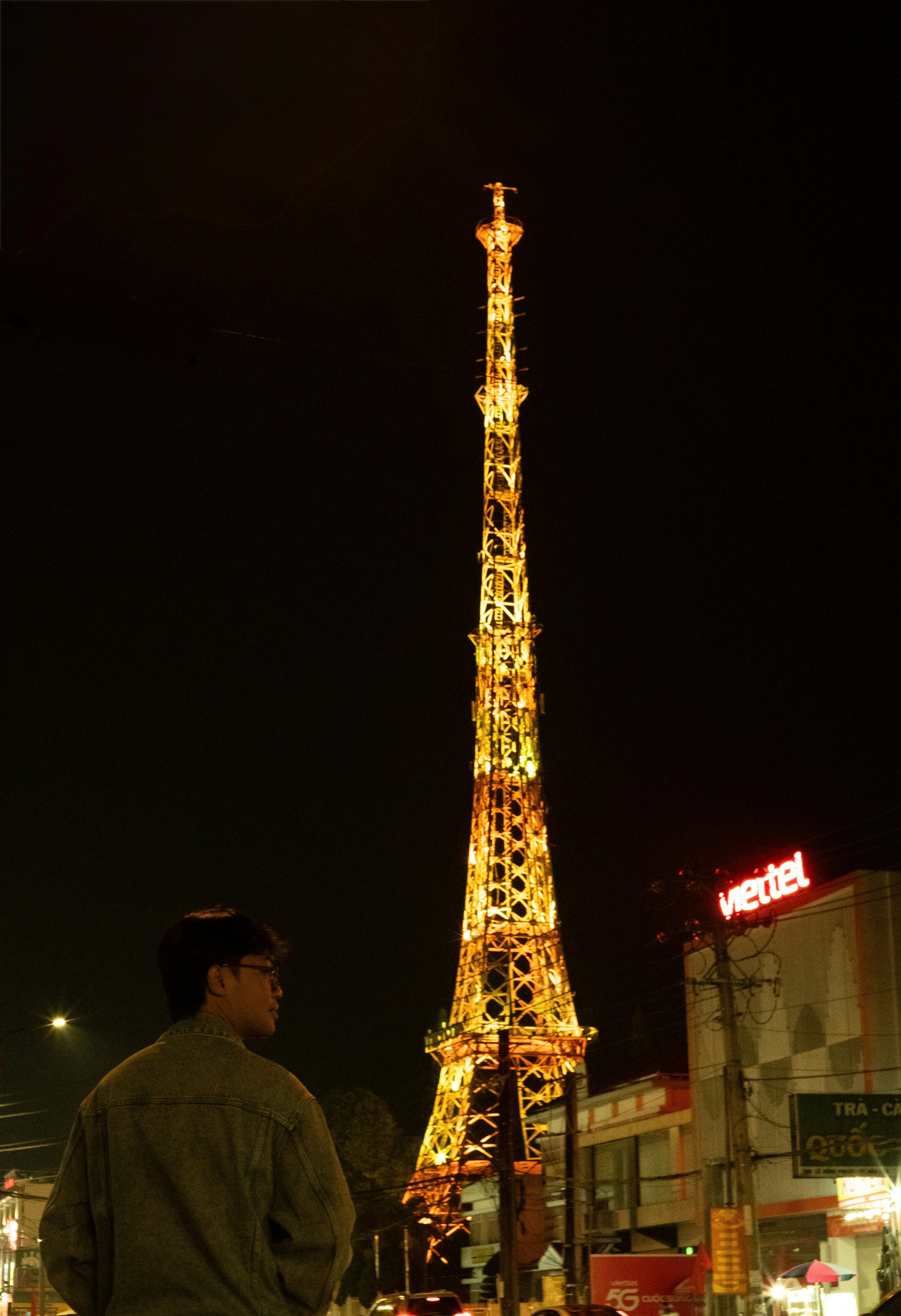 A man looks at a tall, illuminated tower at night.