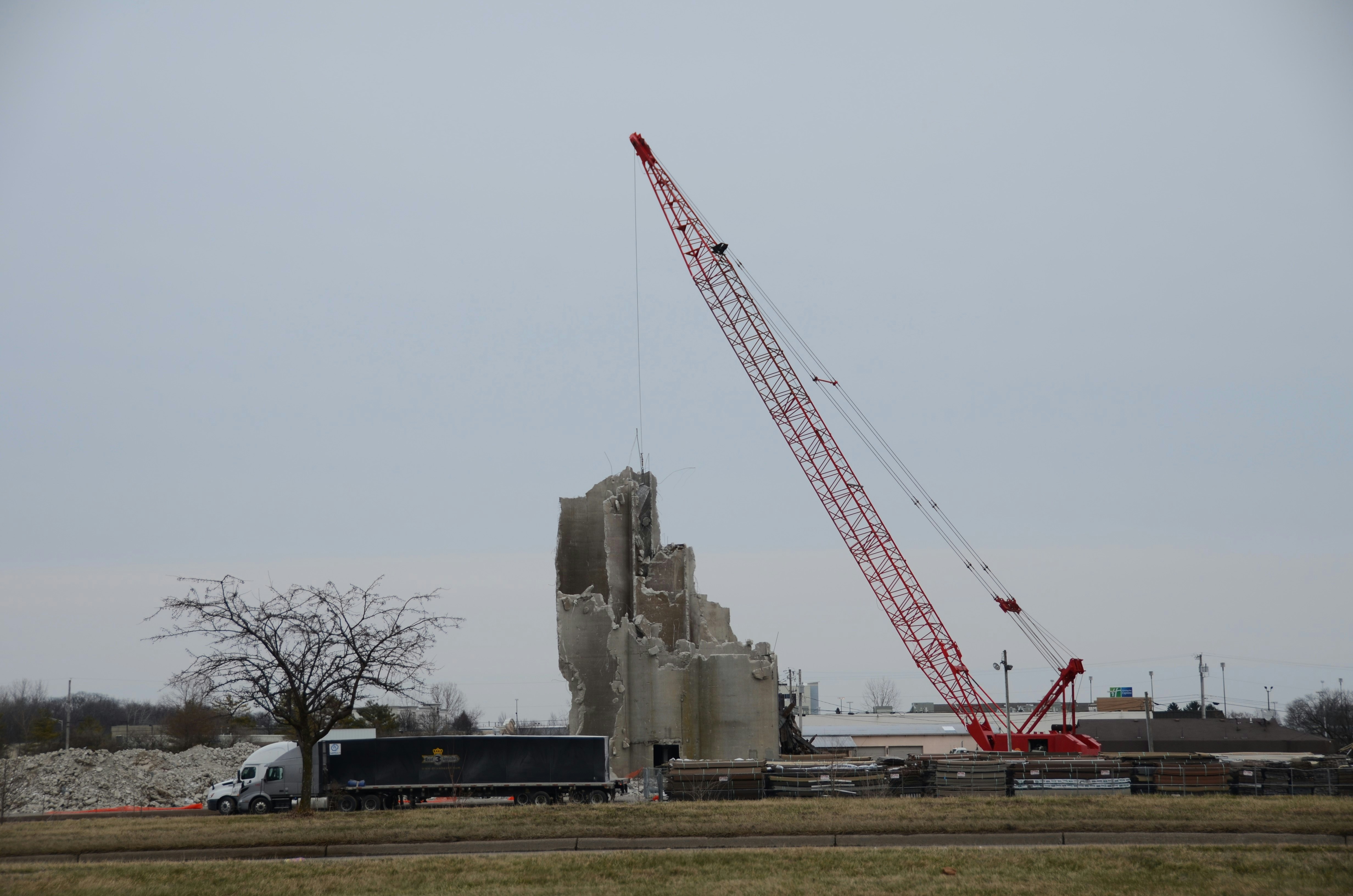 クレーンが近くにトラックを置いて高いコンクリート構造物を壊している。