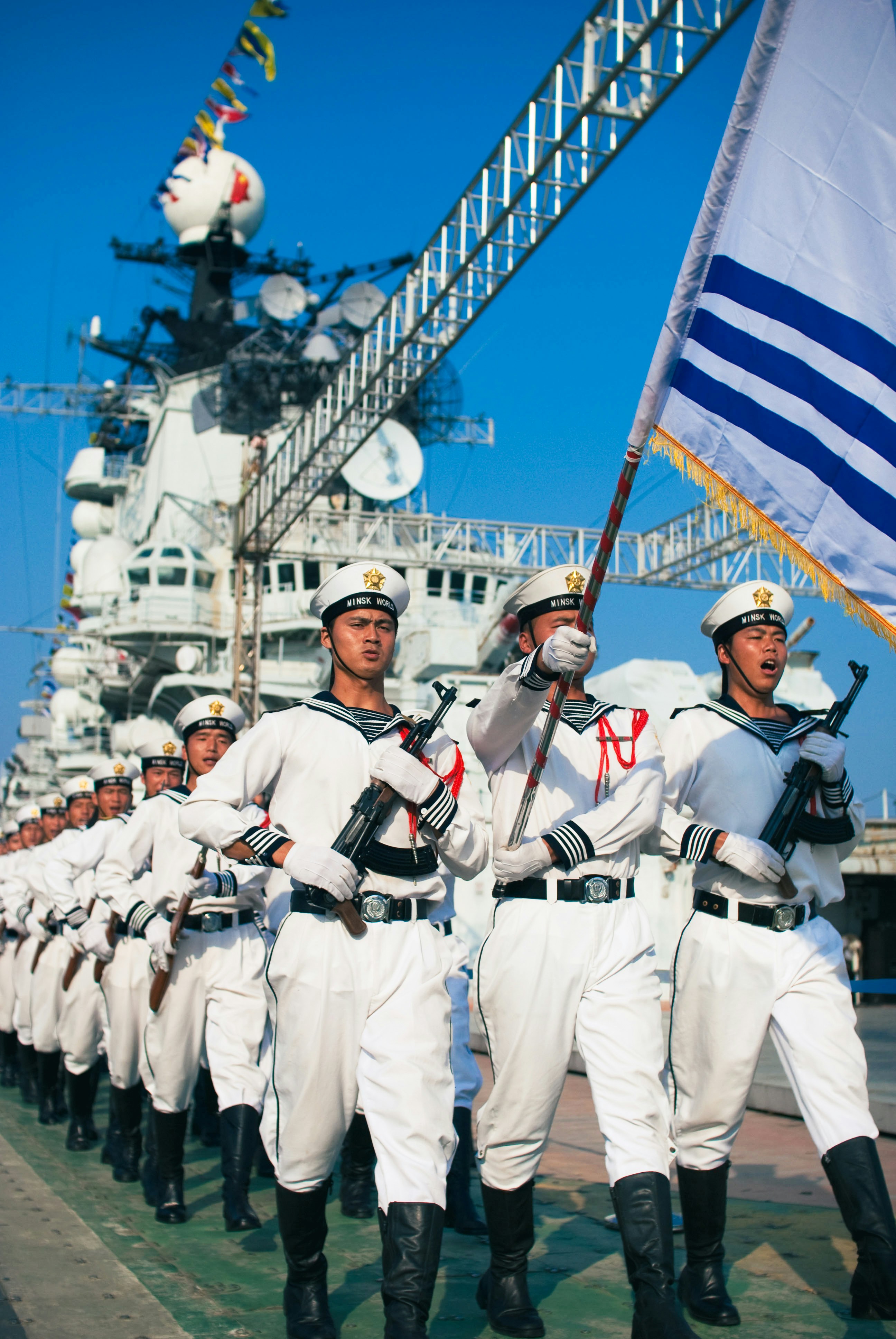 Des marins en uniforme blanc marchent avec un drapeau.