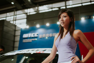 A woman in a purple top poses by a car.