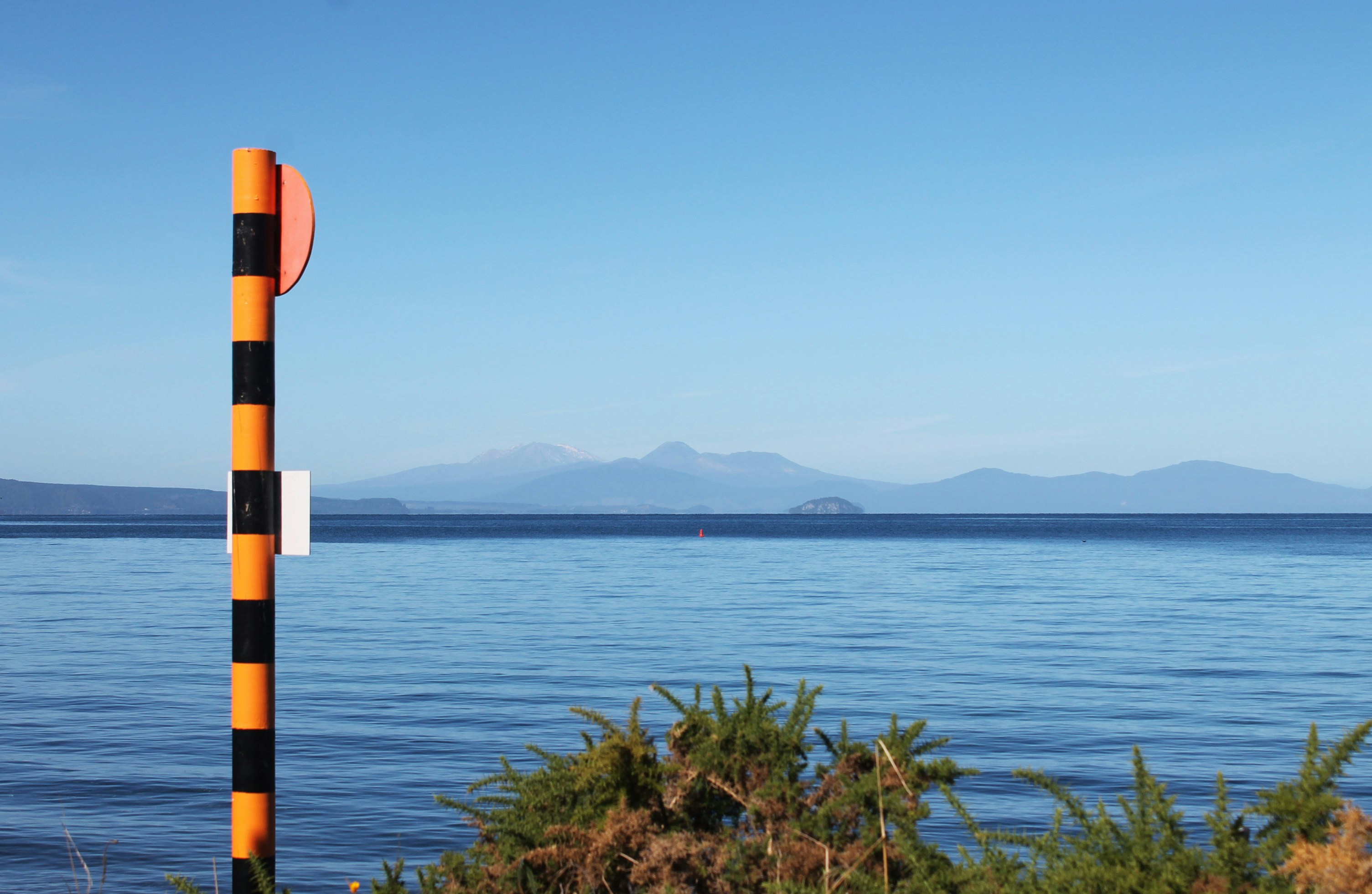 Polo naranja y negro junto a aguas y montañas azules tranquilas.
