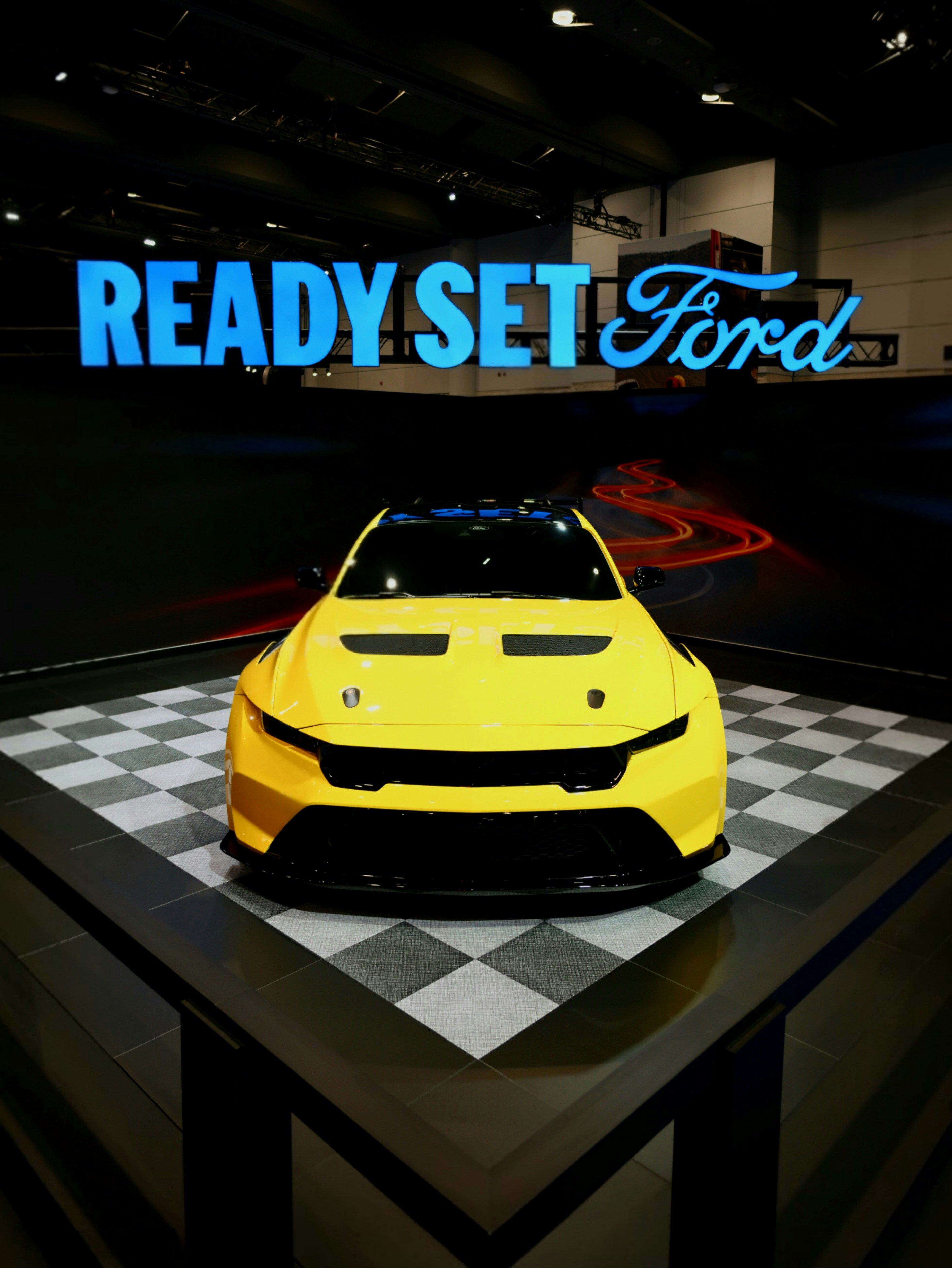 Yellow ford race car on display with checkered flooring.