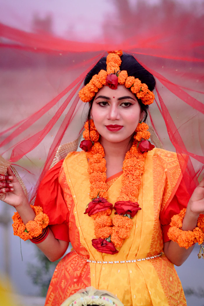Woman adorned with marigold flowers and a red veil at a haldi function