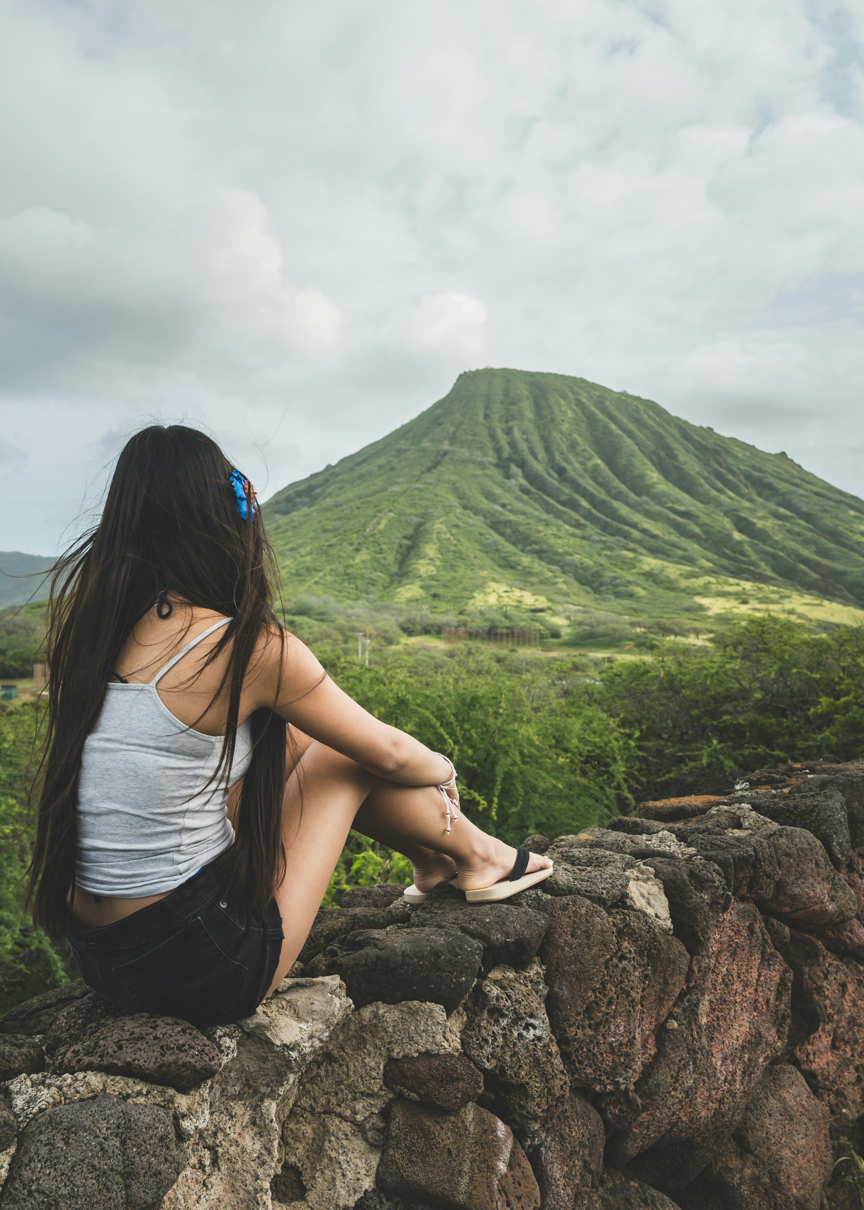 Mulher sentada em um muro de pedra com vista para a montanha verde