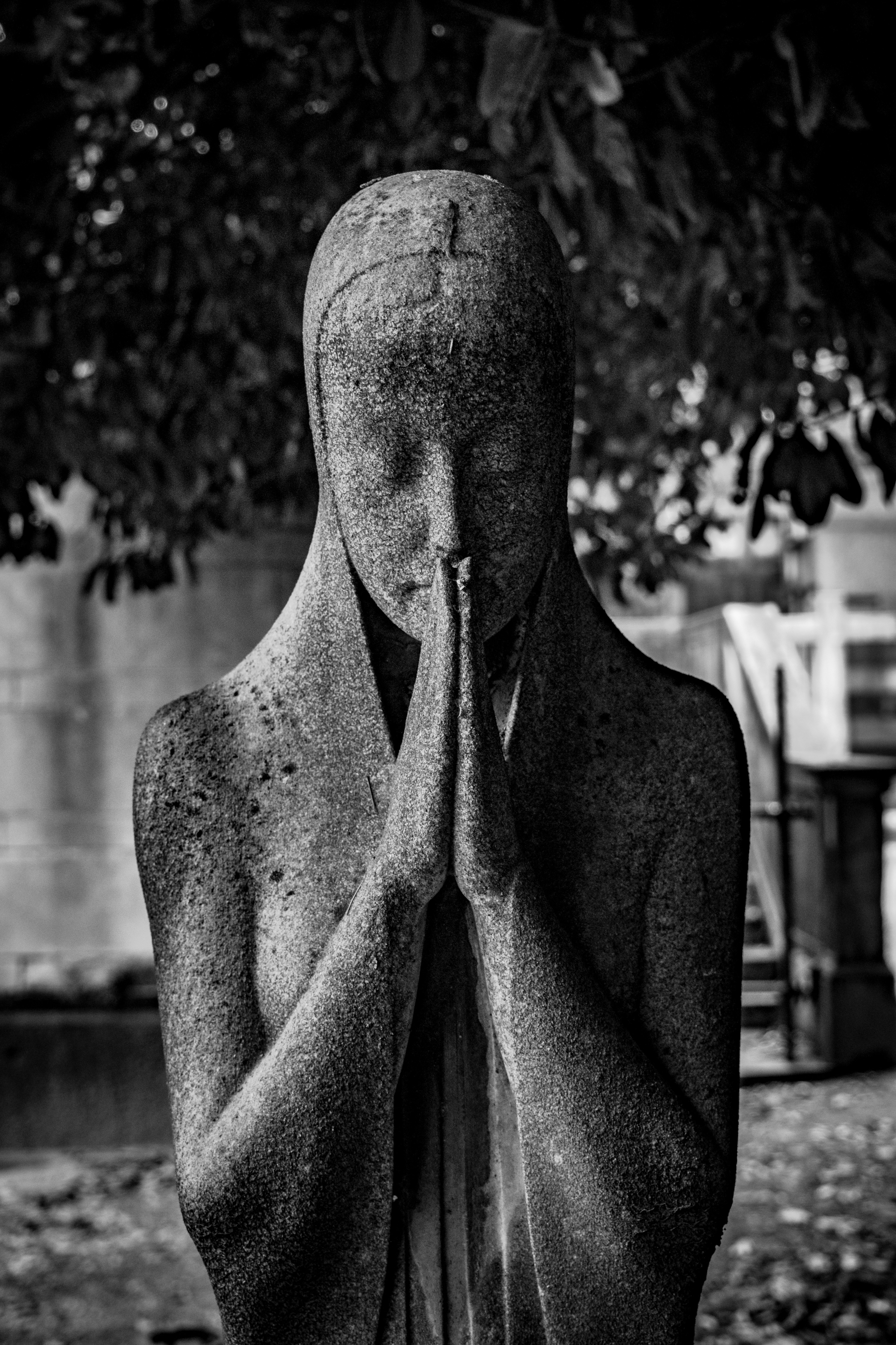 Statua di pietra di una figura in preghiera in un giardino.