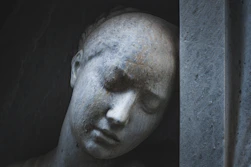 Close-up of a weathered stone sculpture of a sad woman.