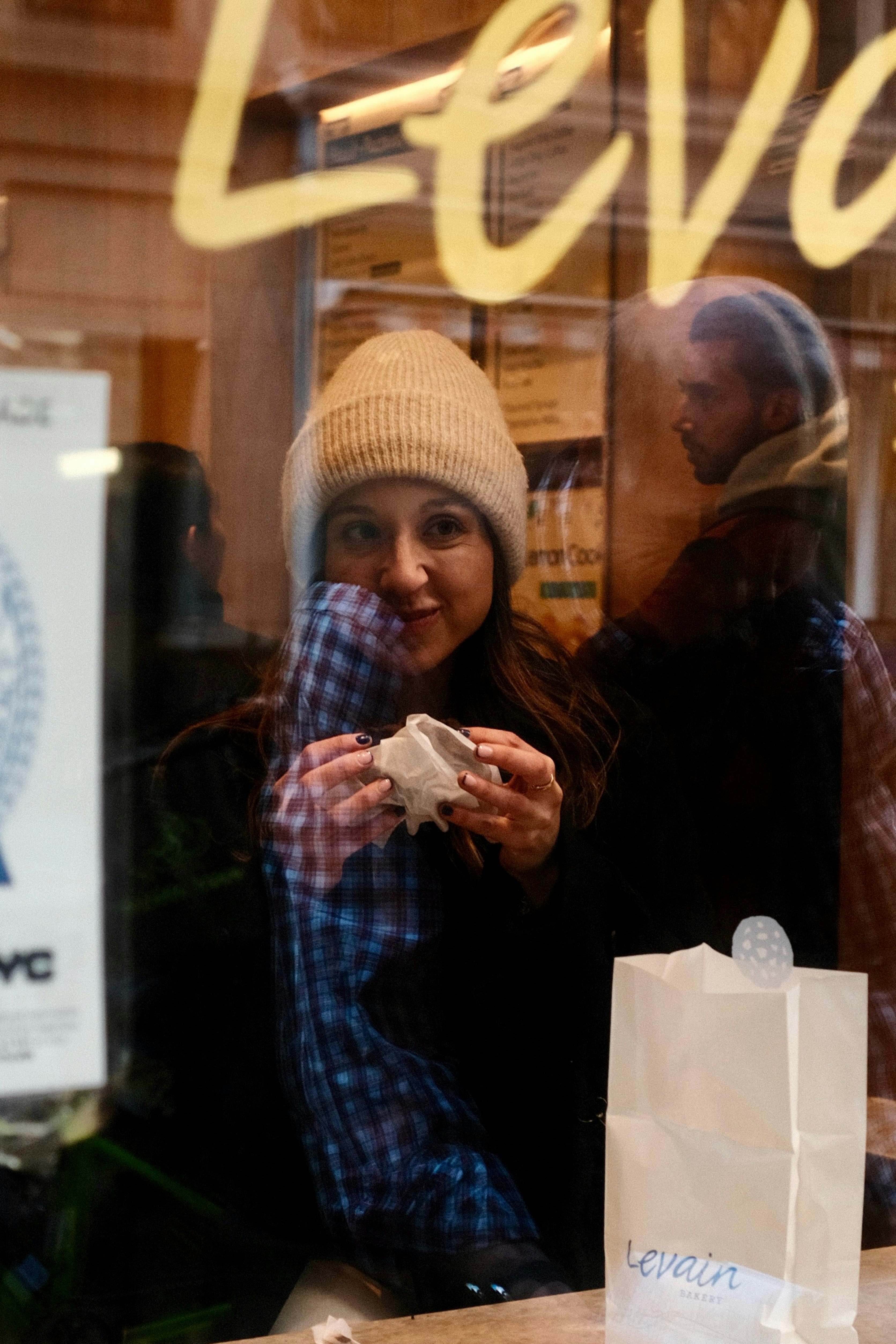Mujer comiendo pasteles a través del reflejo de la ventana de la panadería
