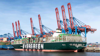 Large container ship docked at a busy port with cranes.