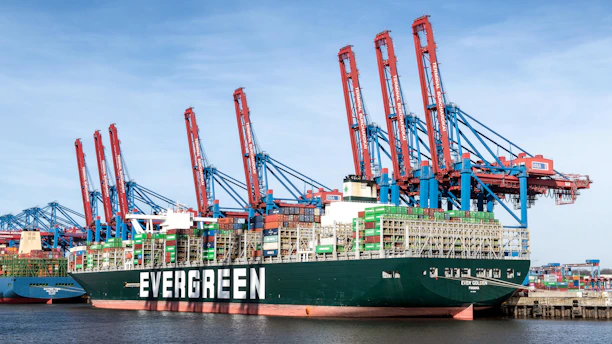 Large container ship docked at a busy port with cranes.