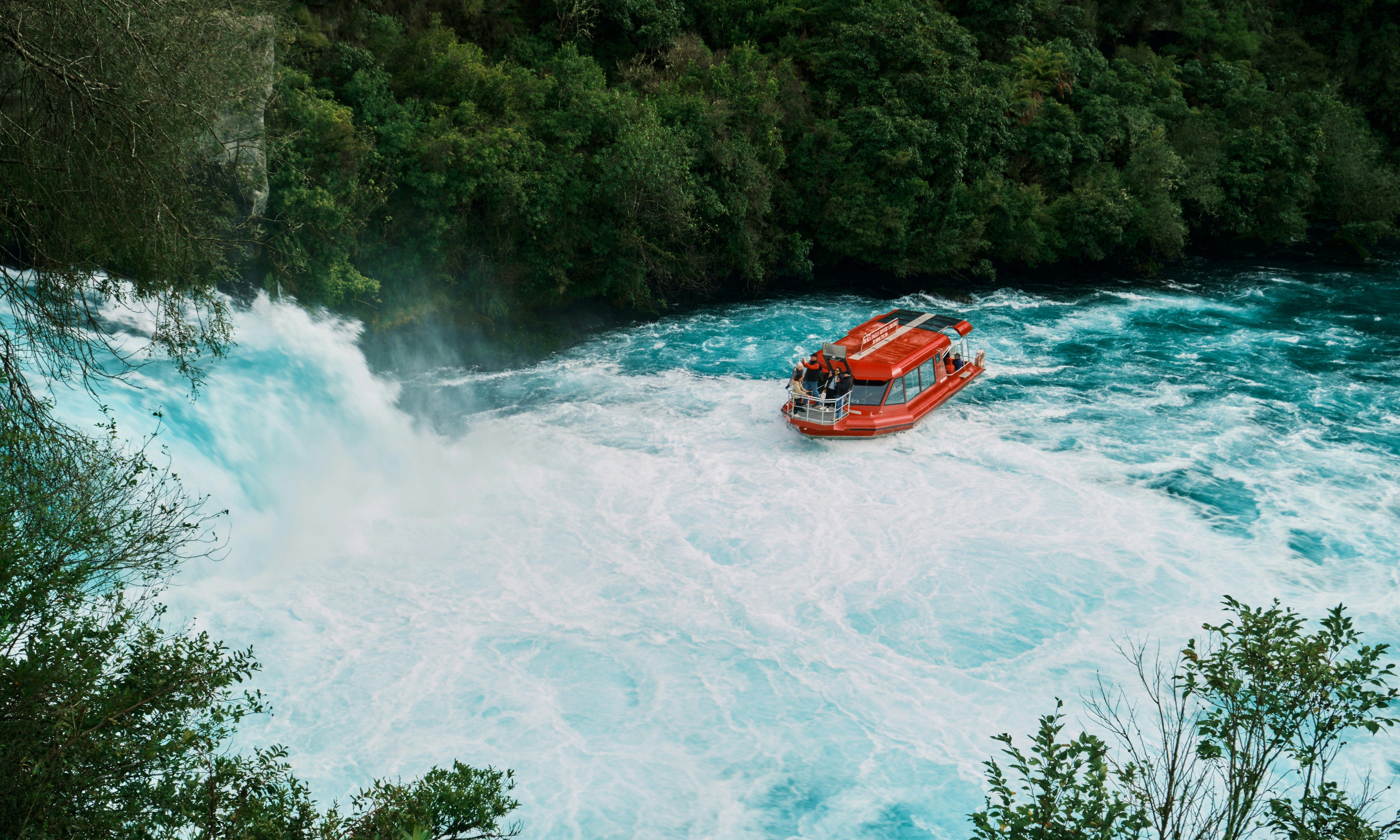 Orange boat navigates powerful rapids near waterfall