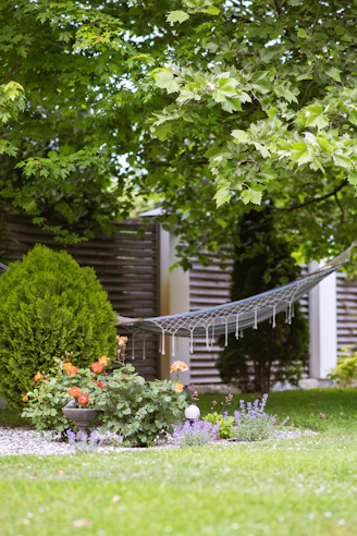 Hammock hanging in a lush green garden with flowers.