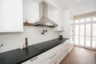 Modern white kitchen with black countertop and stainless steel hood.