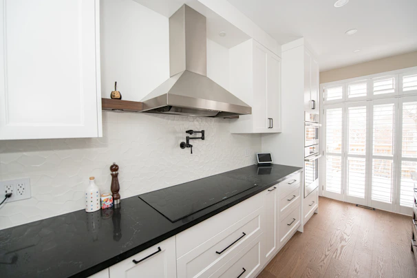 Modern white kitchen with black countertop and stainless steel hood.
