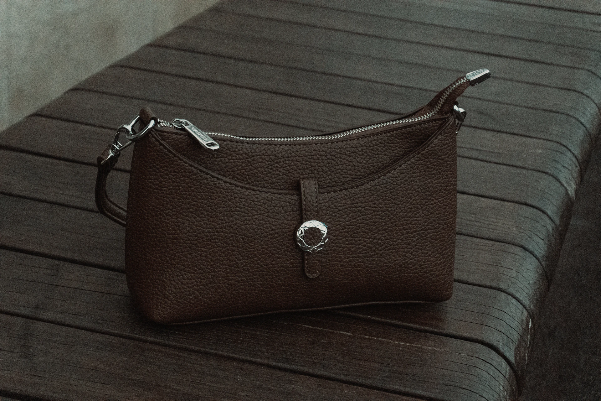 A brown leather handbag rests on a wooden surface.