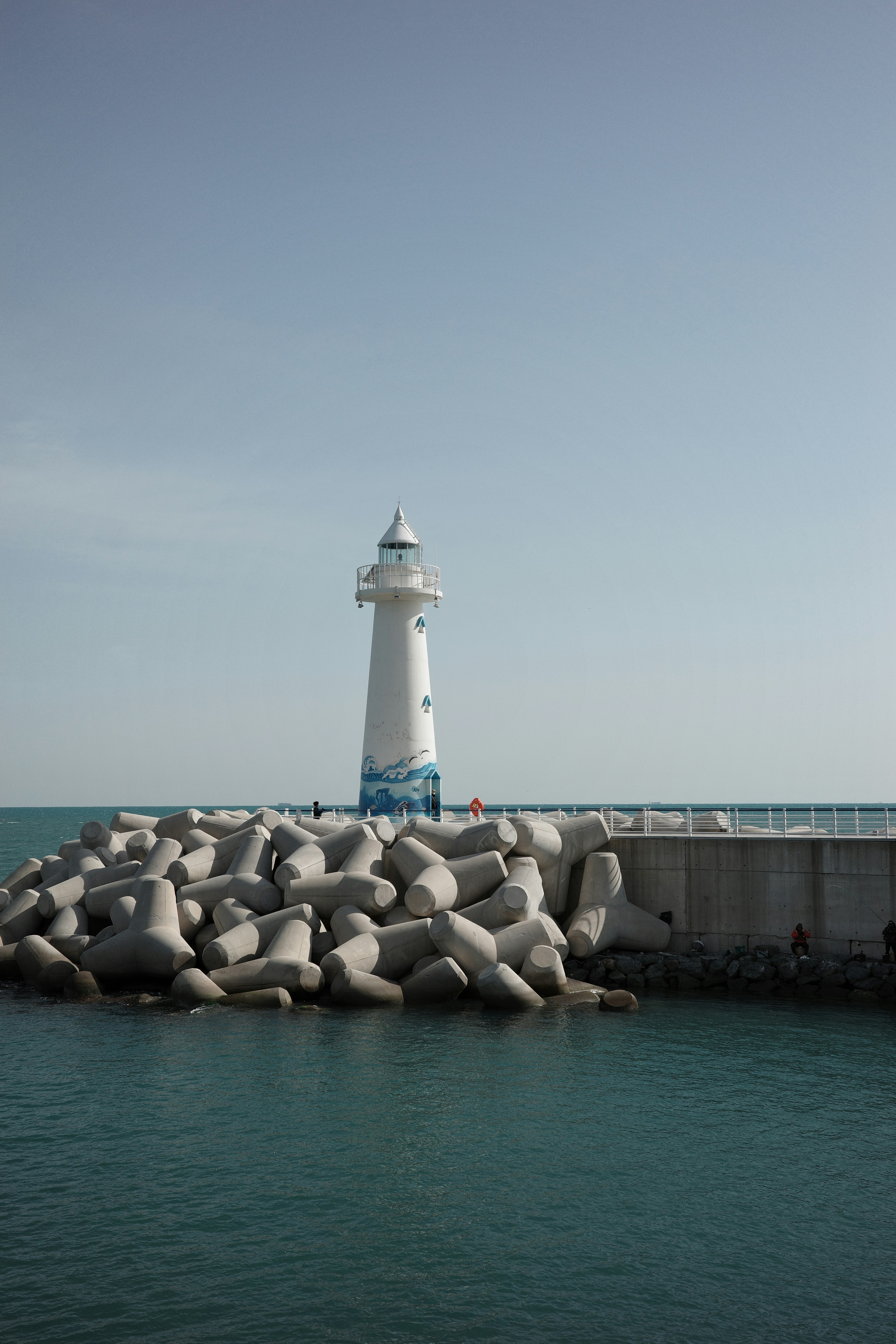 A white lighthouse stands on a breakwater with concrete blocks.