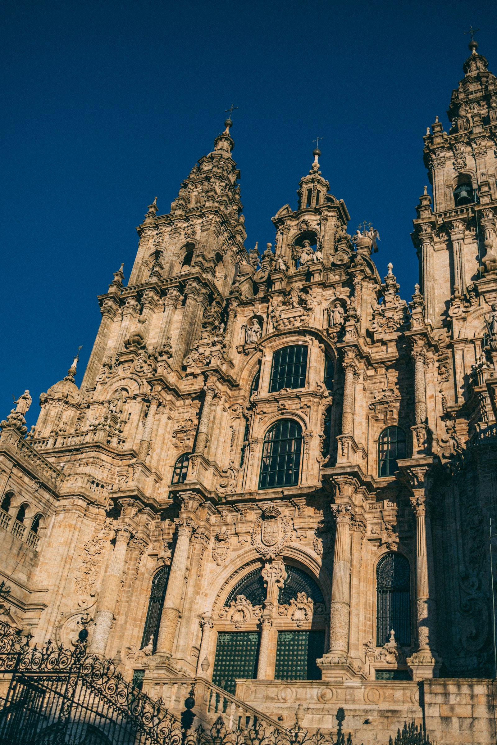 Looking up at the ornate baroque stone towers and sculpted facade of Santiago de Compostela's cathedral against a deep blue sky