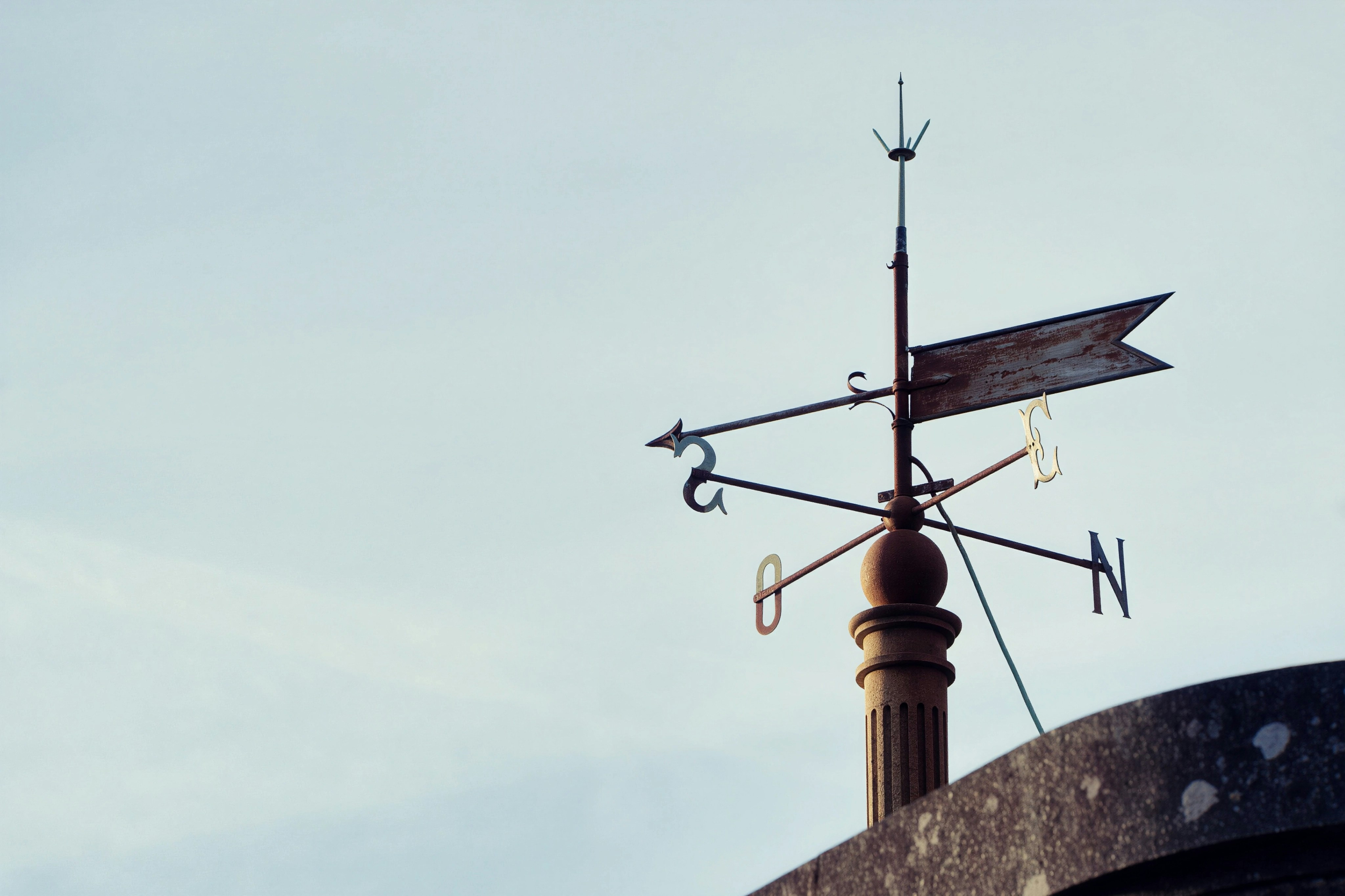 A weathered weathervane points the way on a rooftop.