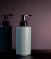 Two pump bottles on a dark shelf