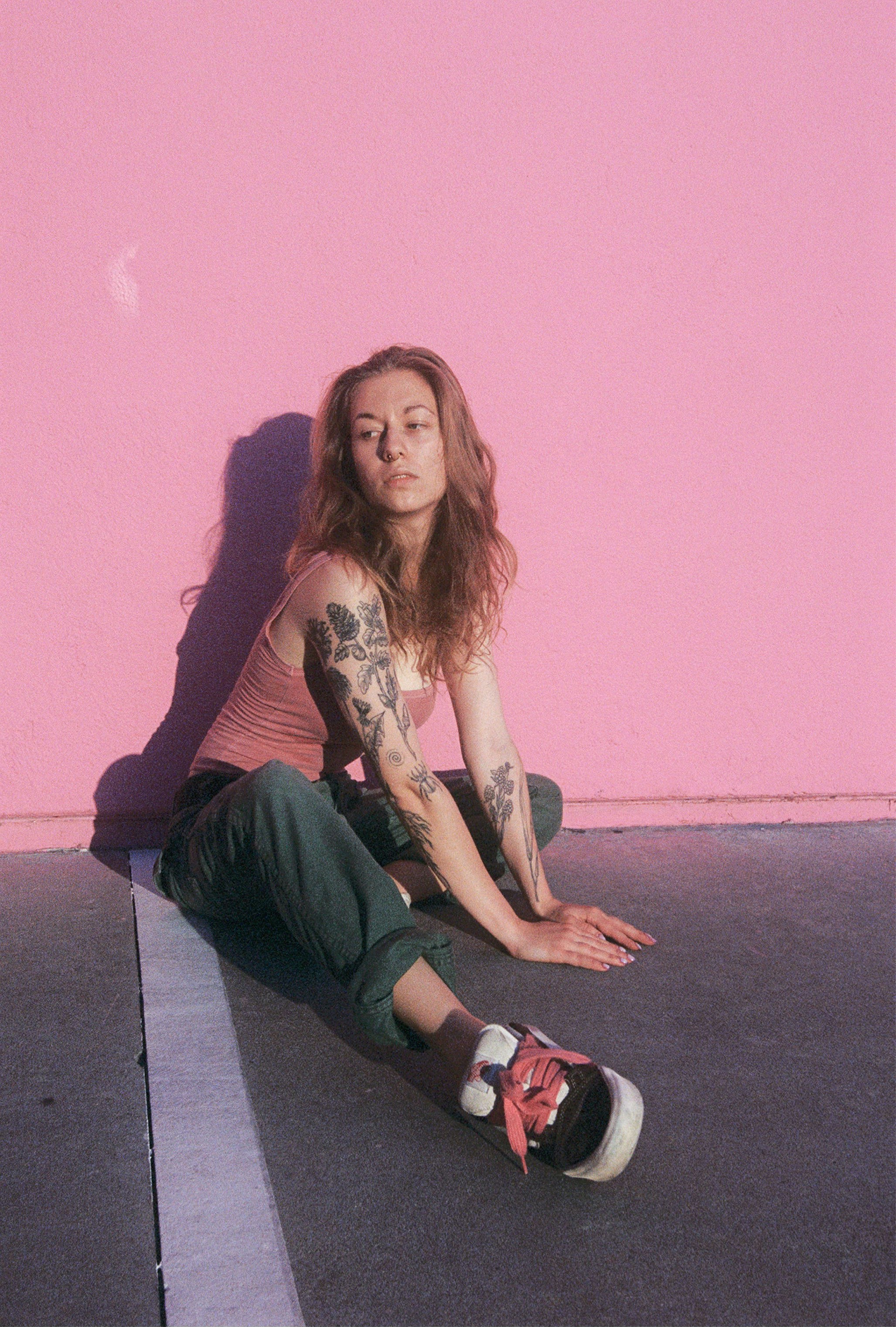 Woman with tattoos sitting against pink wall