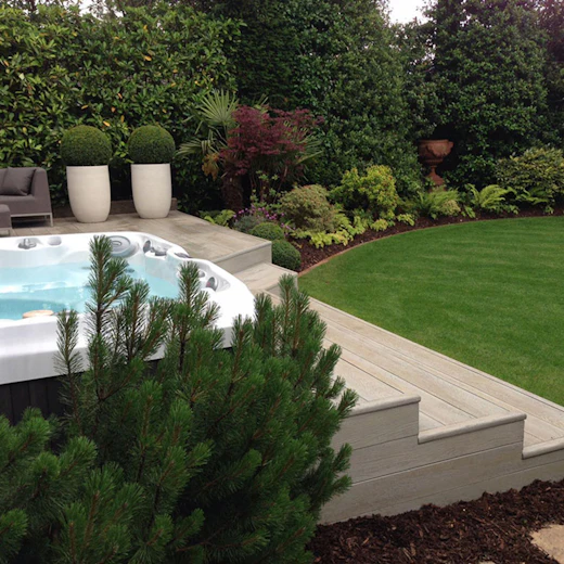 Spa encastré au bord d’une terrasse, dans un jardin paysager.