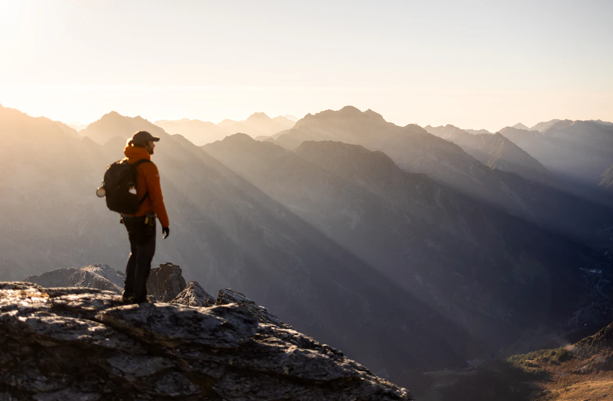 Hiker on mountain peak at sunrise with sun rays.